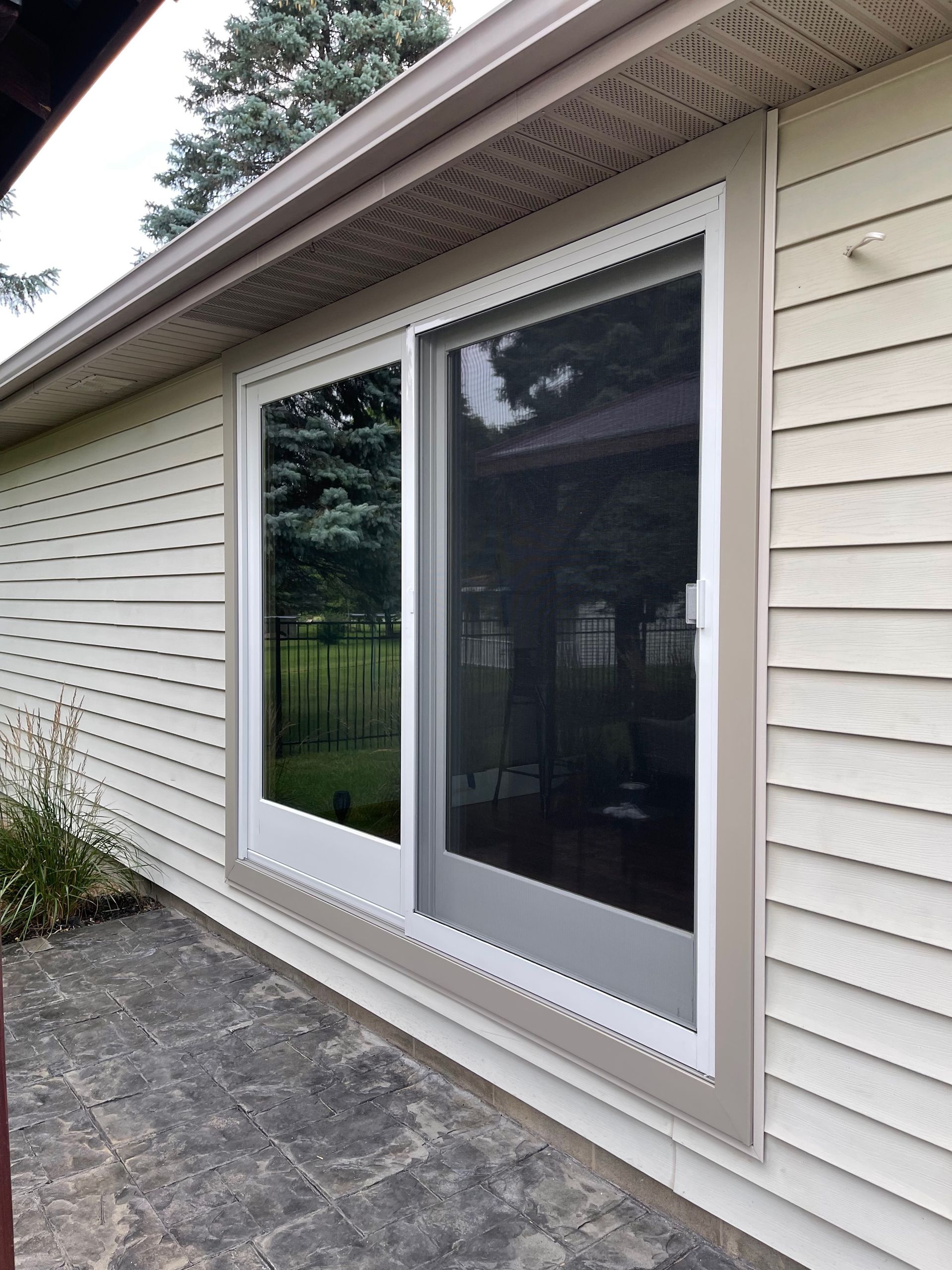 Sliding glass door with white frame, tan trim, and screen on a house with beige siding.