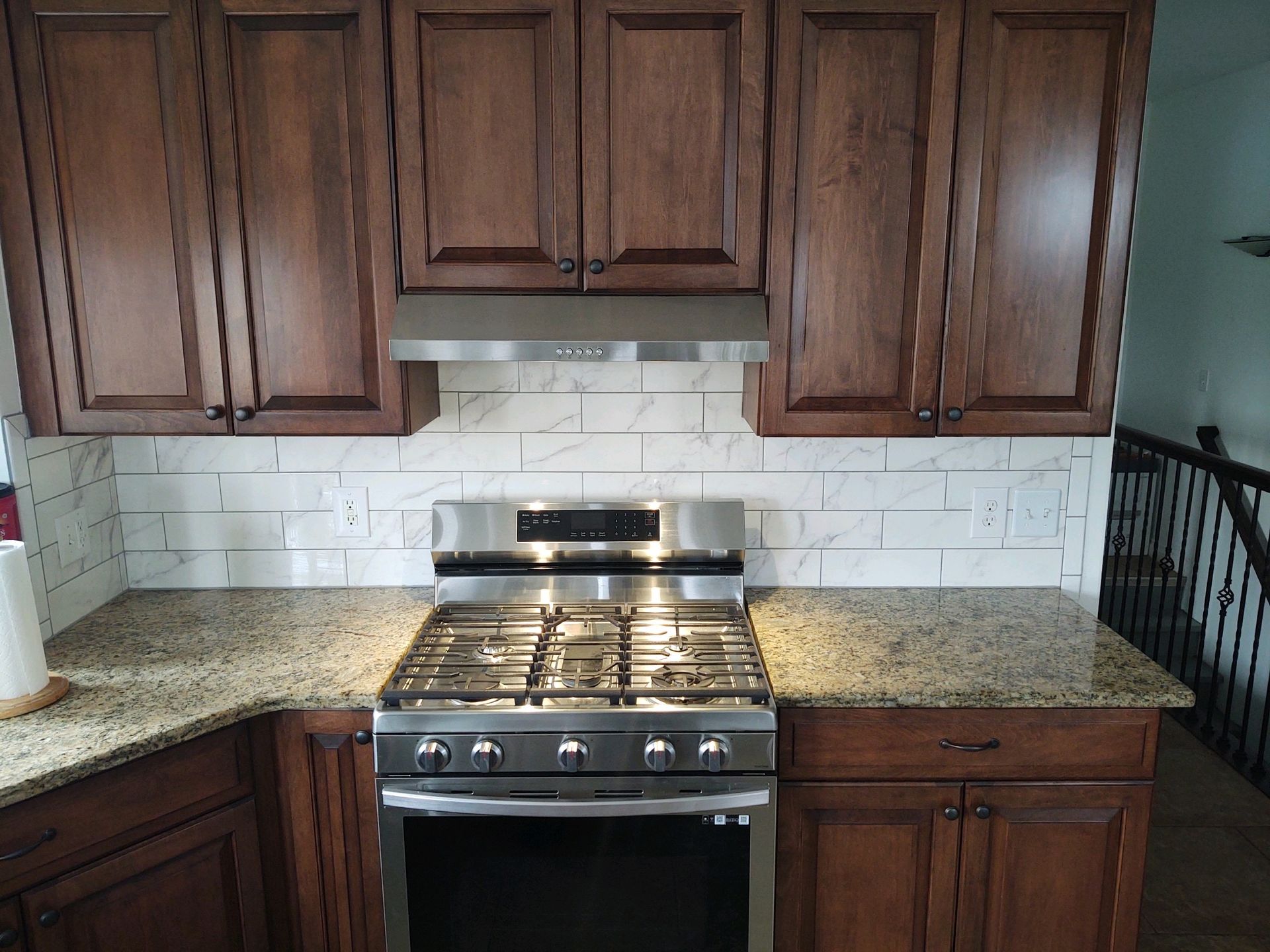 Kitchen with brown cabinets, stainless steel stove, granite countertops, and white tile backsplash.