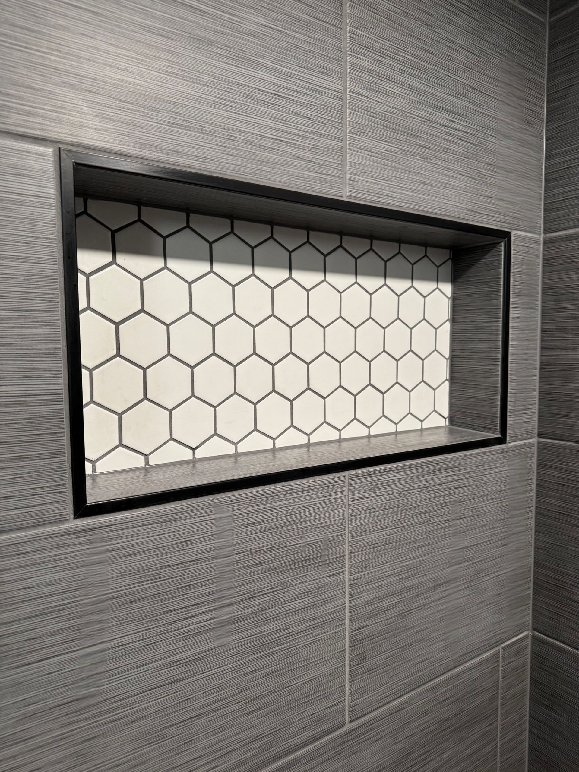 Recessed shower shelf with black frame, hexagonal white and gray tile. Gray wall tile.