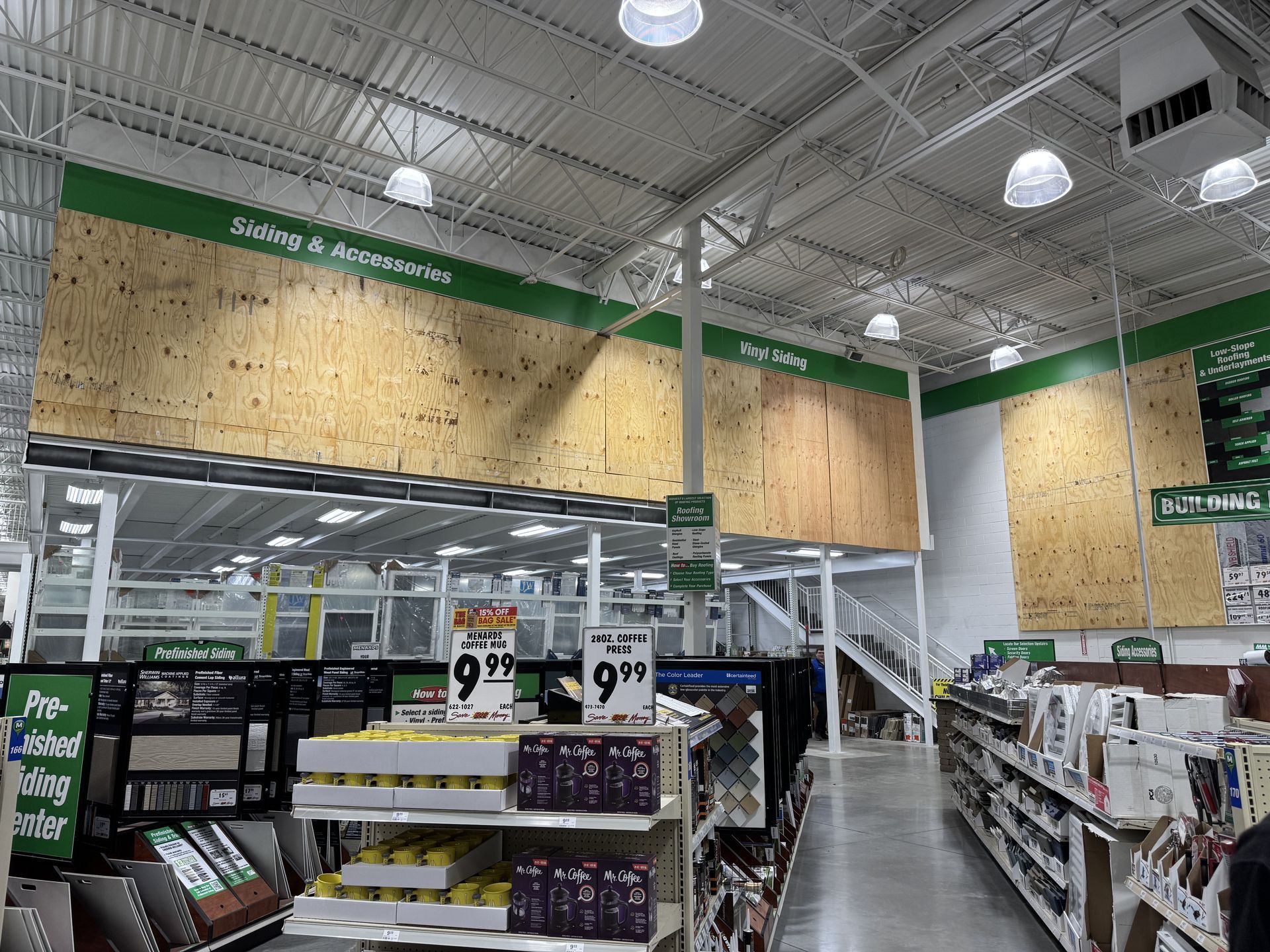 Inside a large hardware store, wood displays under signs, white ceiling, products on shelves below.