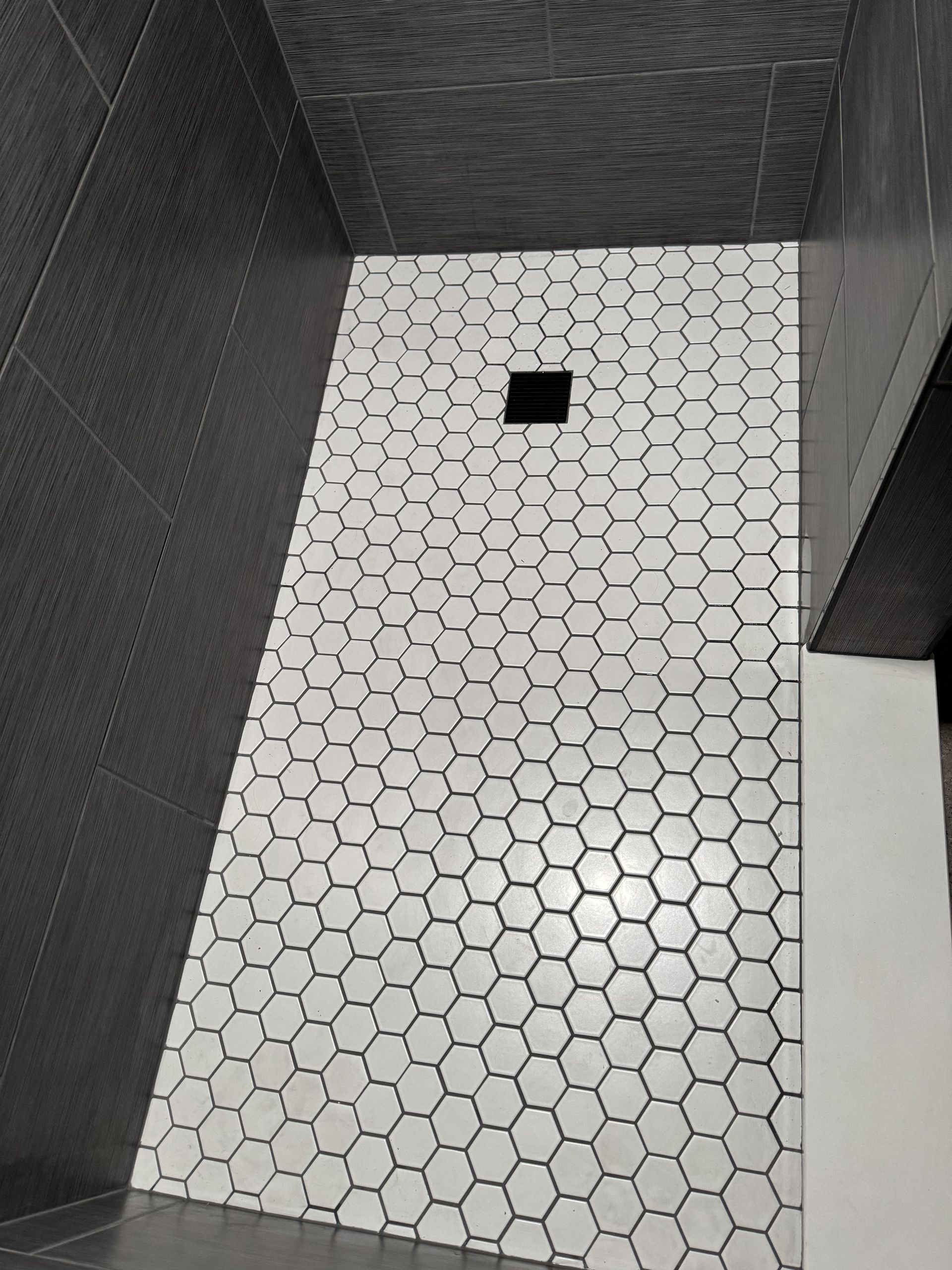 Bathroom shower with hexagonal white tile floor, dark gray walls, and a drain.