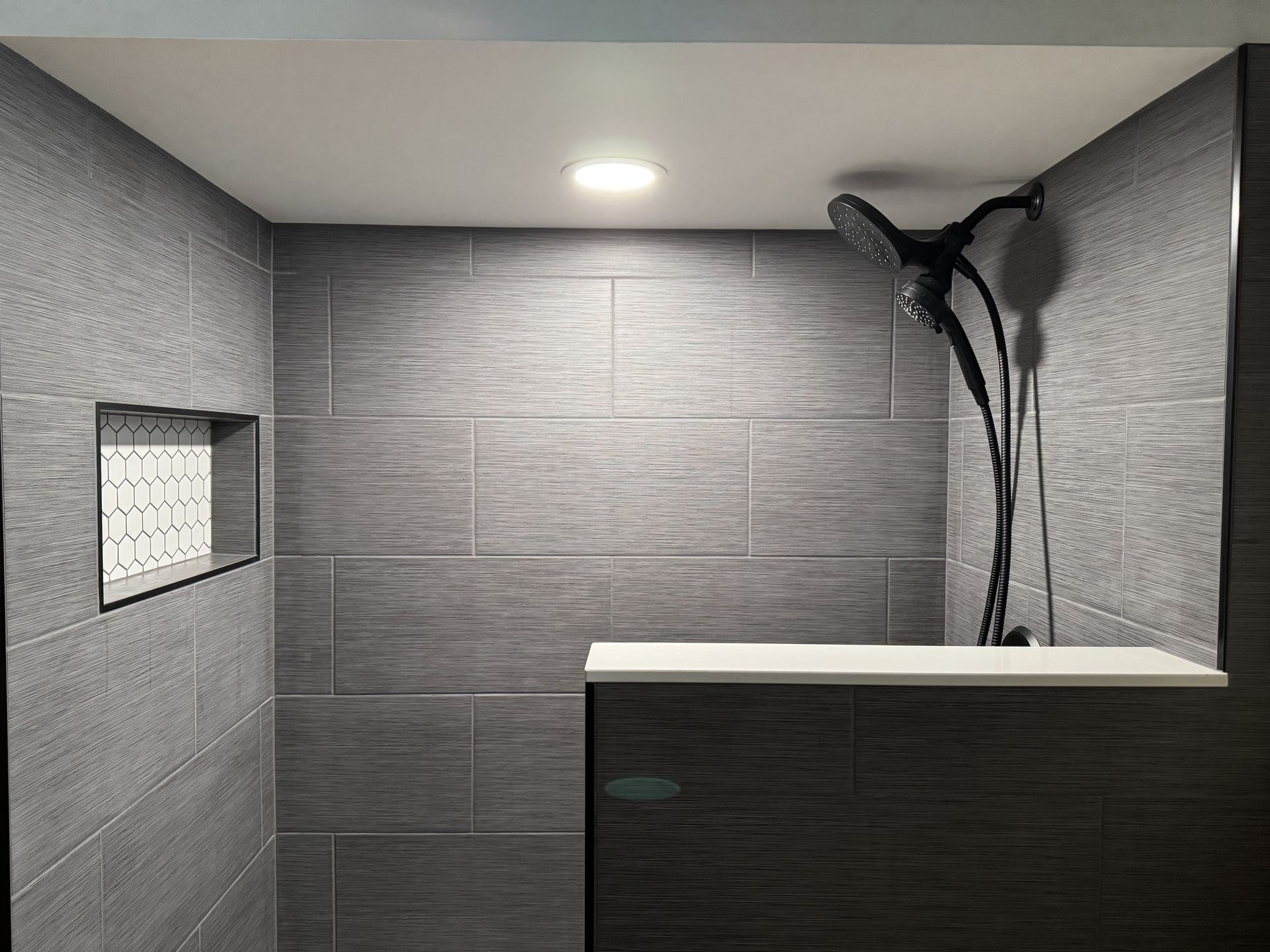 Gray tiled shower with built-in bench, recessed shelf, and black showerhead.