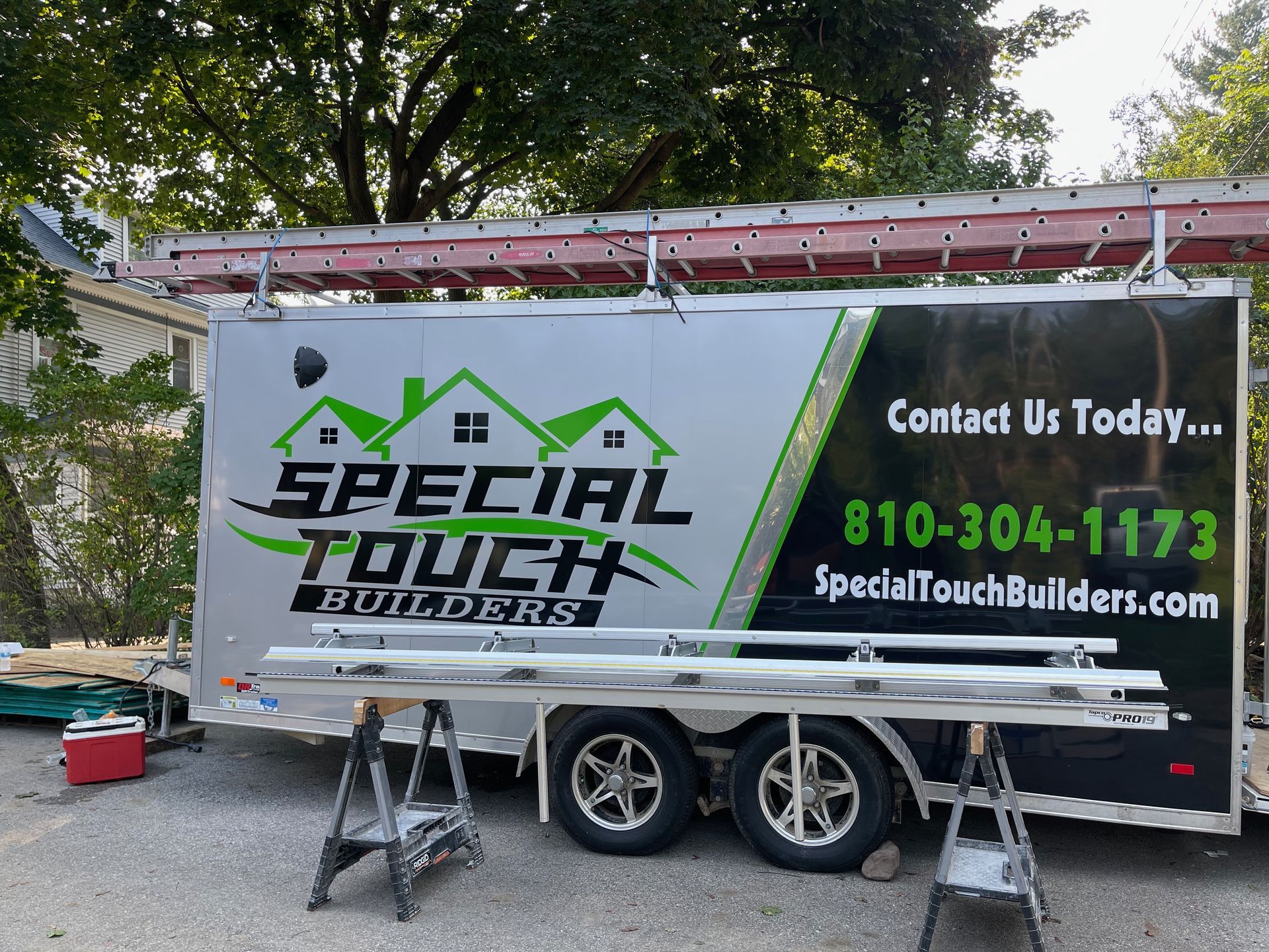Special Touch Builders trailer with ladder on top and materials on sawhorses.