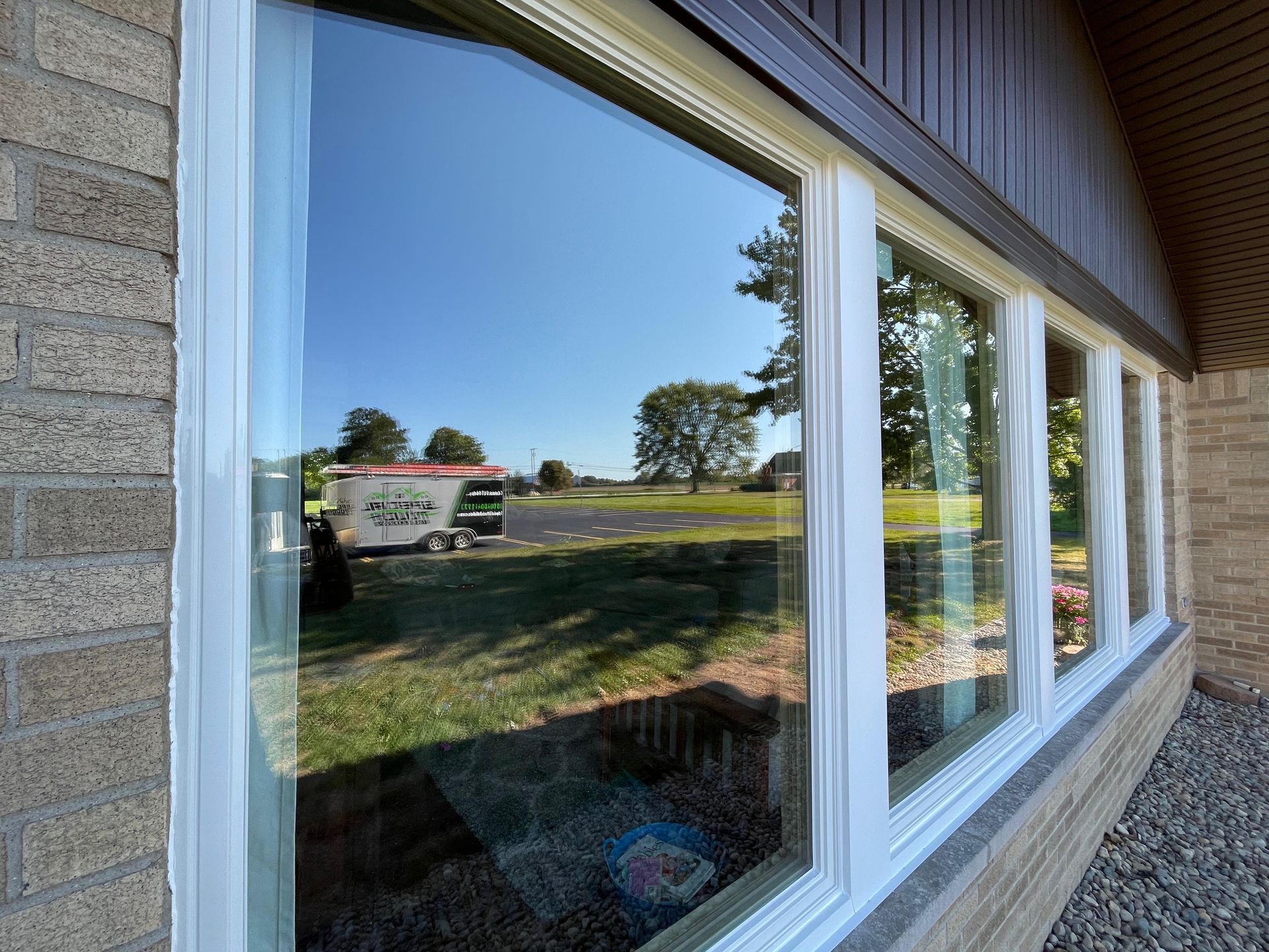 Windows reflecting a sunny outdoor scene, white frames, brick and siding exterior.