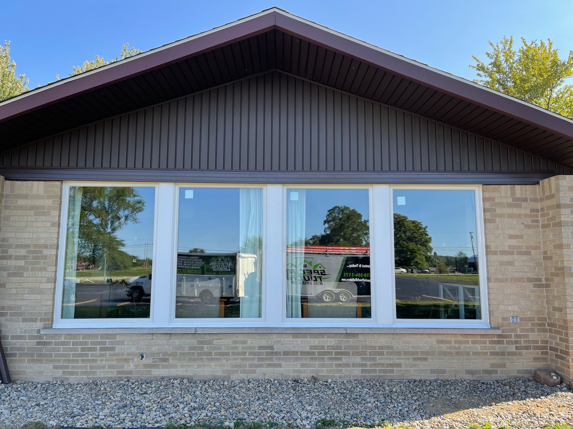 Newly installed white-framed windows on a brick building with brown trim. Reflections of sky and trees are visible.