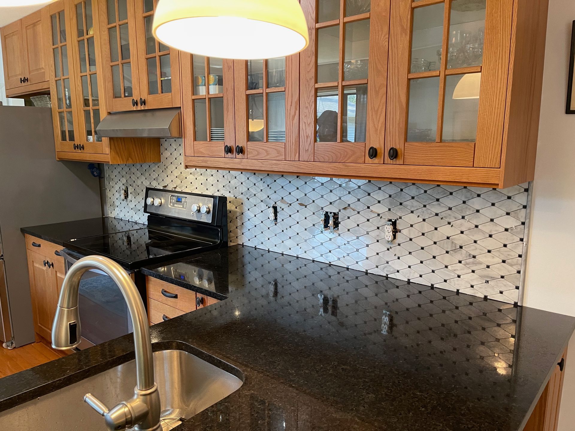 Kitchen with wooden cabinets, black granite countertops, stainless steel sink, and decorative backsplash.