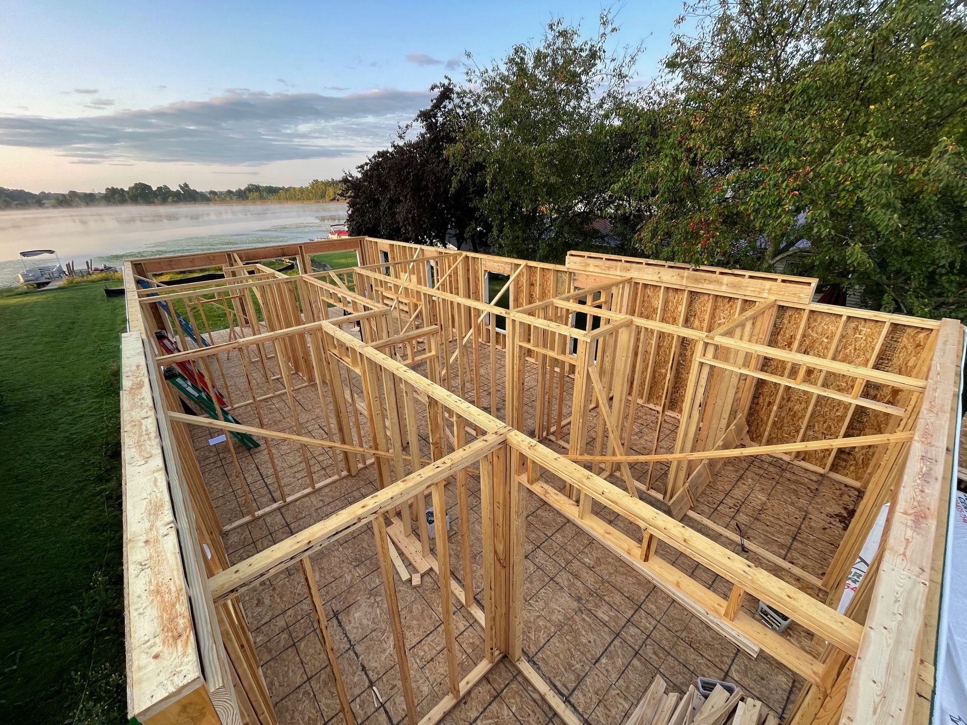 Wooden frame of a building under construction, overlooking a lake at sunset.