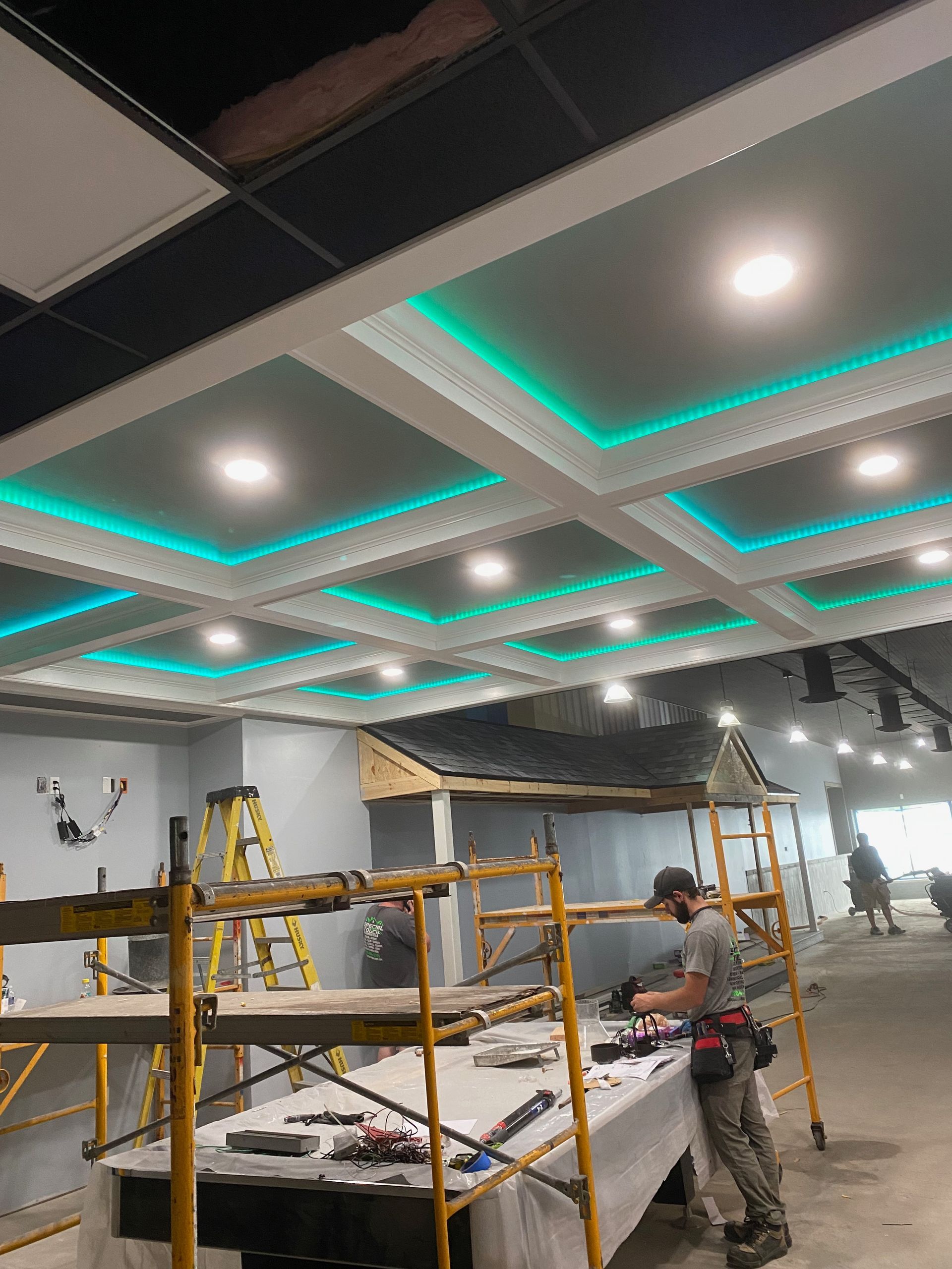Construction site with a detailed ceiling design including LED lighting and a worker installing equipment.
