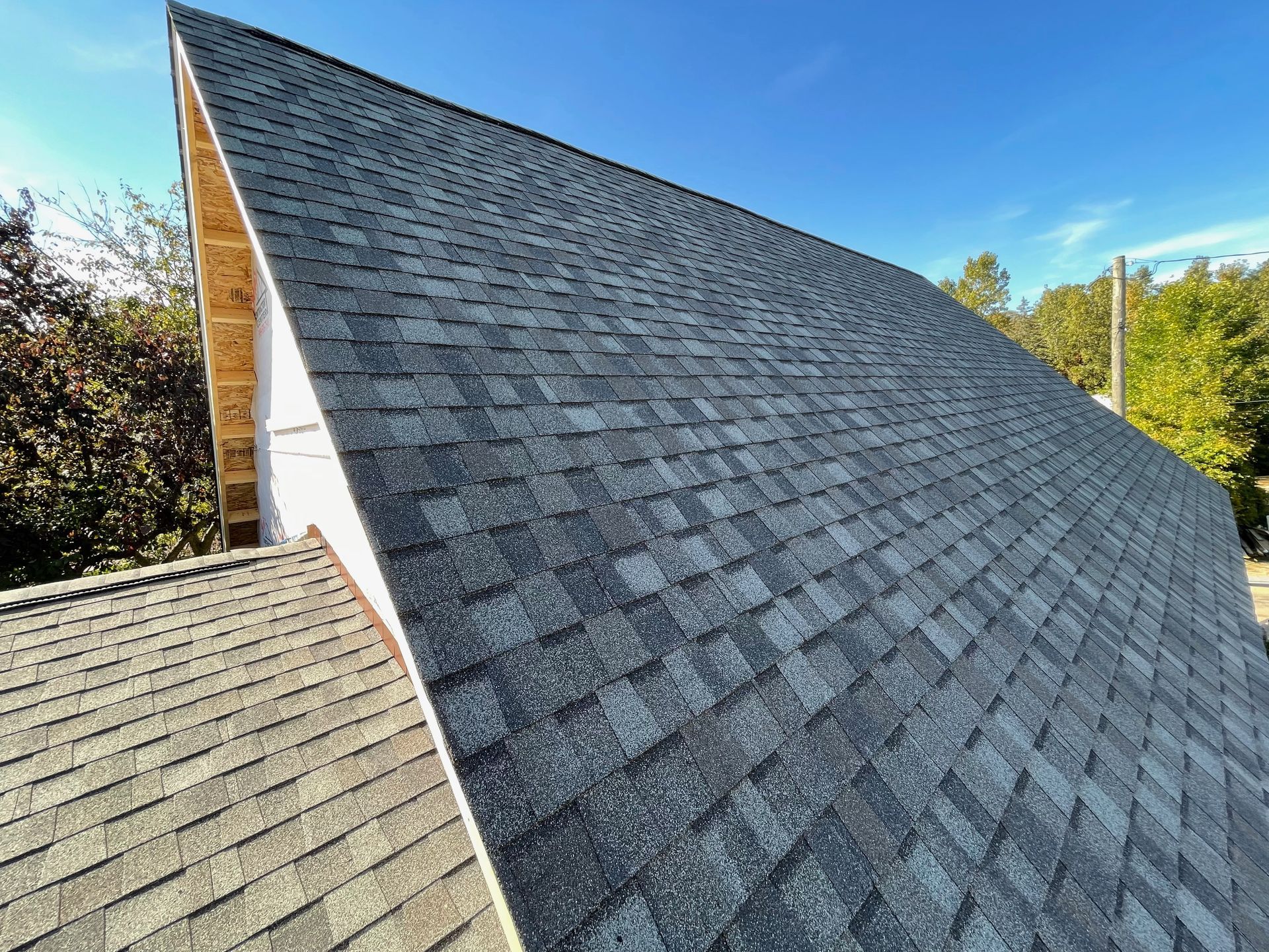 Gray shingle roof, angled, against a blue sky, under construction, with exposed wood.