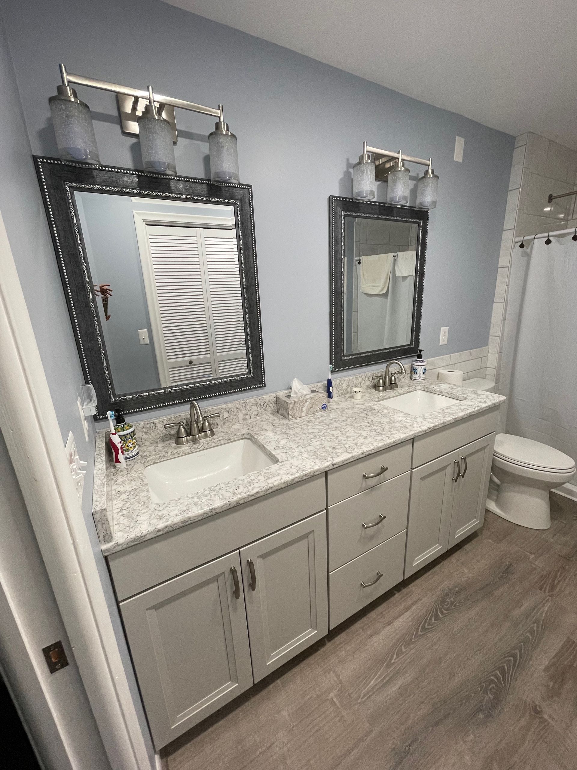 Bathroom with dual sinks, mirrors, grey cabinets, white countertop, and light blue walls.