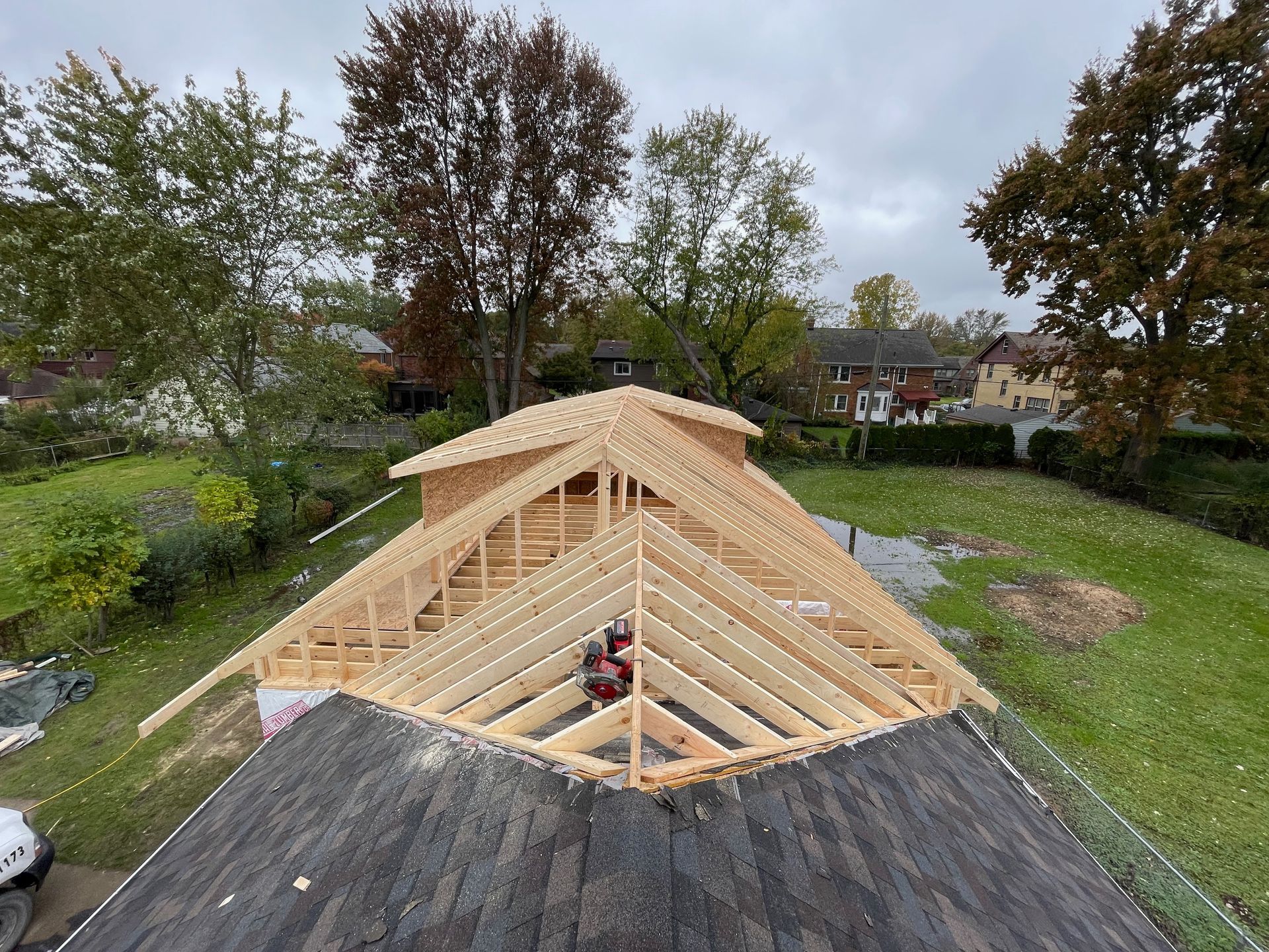 Wooden roof framework under construction on top of an older roof, with trees in the background.