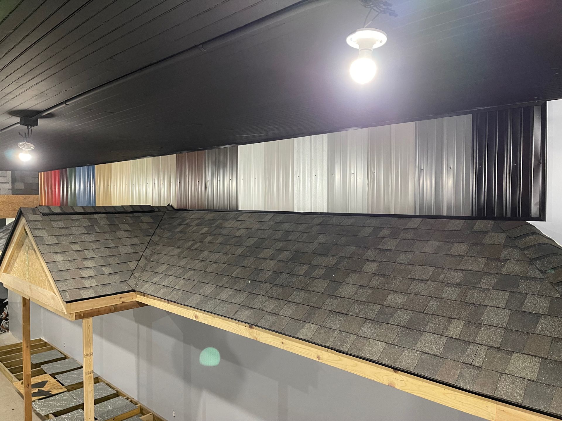 A display of various roofing materials: asphalt shingles and metal panels in different colors.