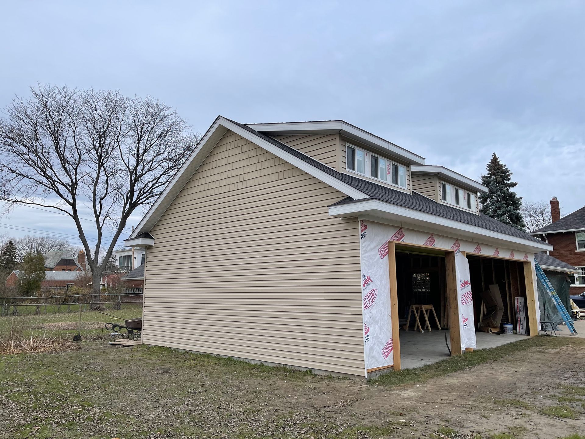 Beige-sided two-car garage under construction with roof and window dormers.