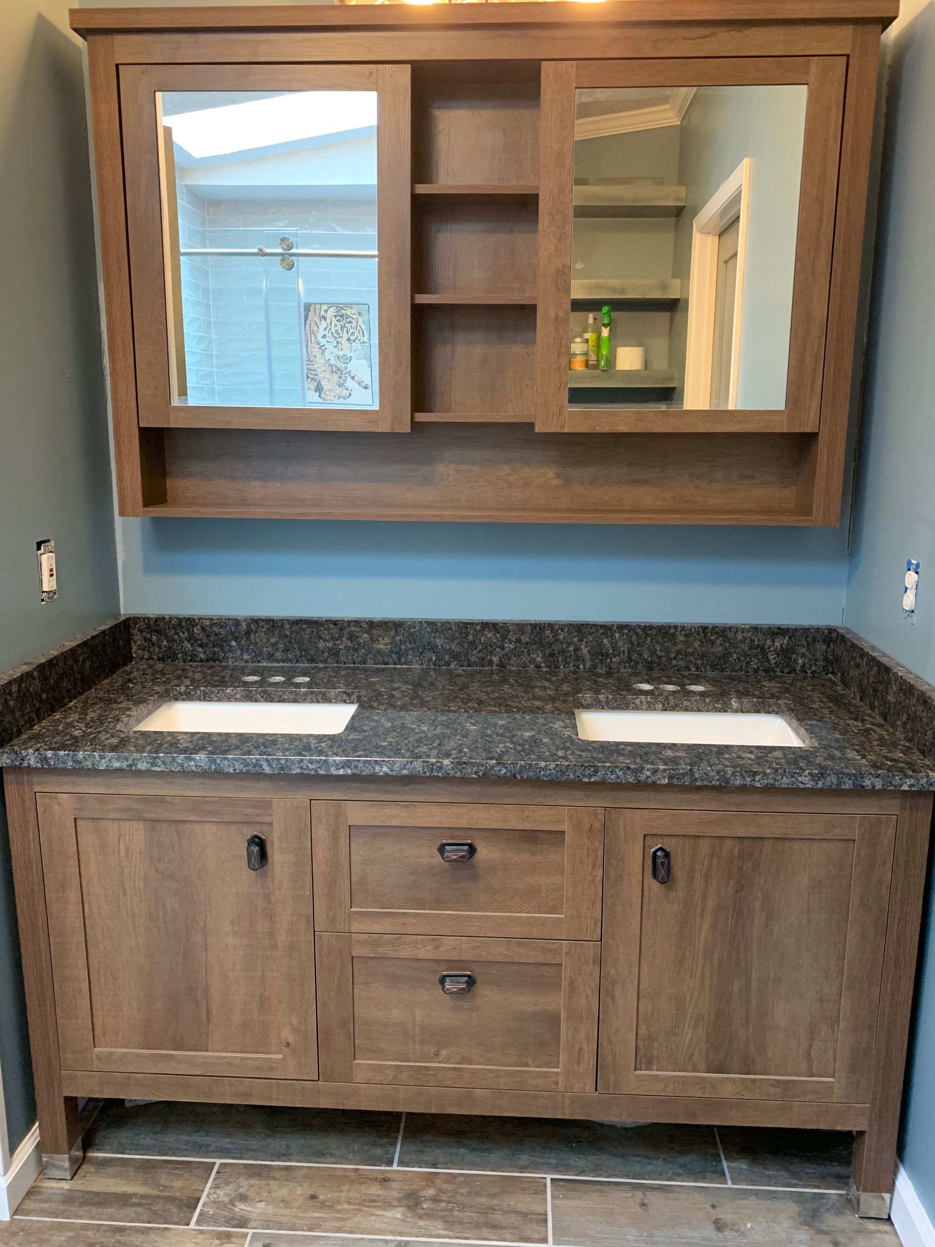 Bathroom vanity with dark granite countertop, two sinks, and a wooden medicine cabinet.