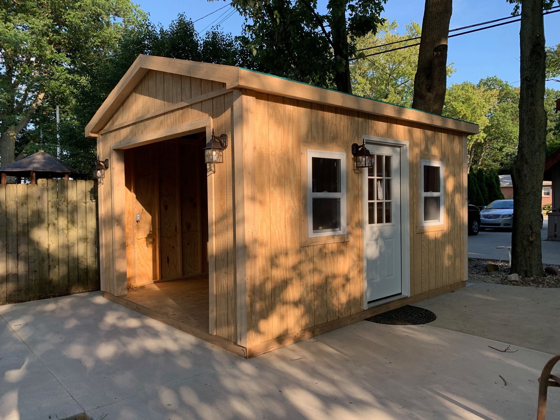 Wooden shed with open garage space, two windows, and a door, set on a concrete pad.