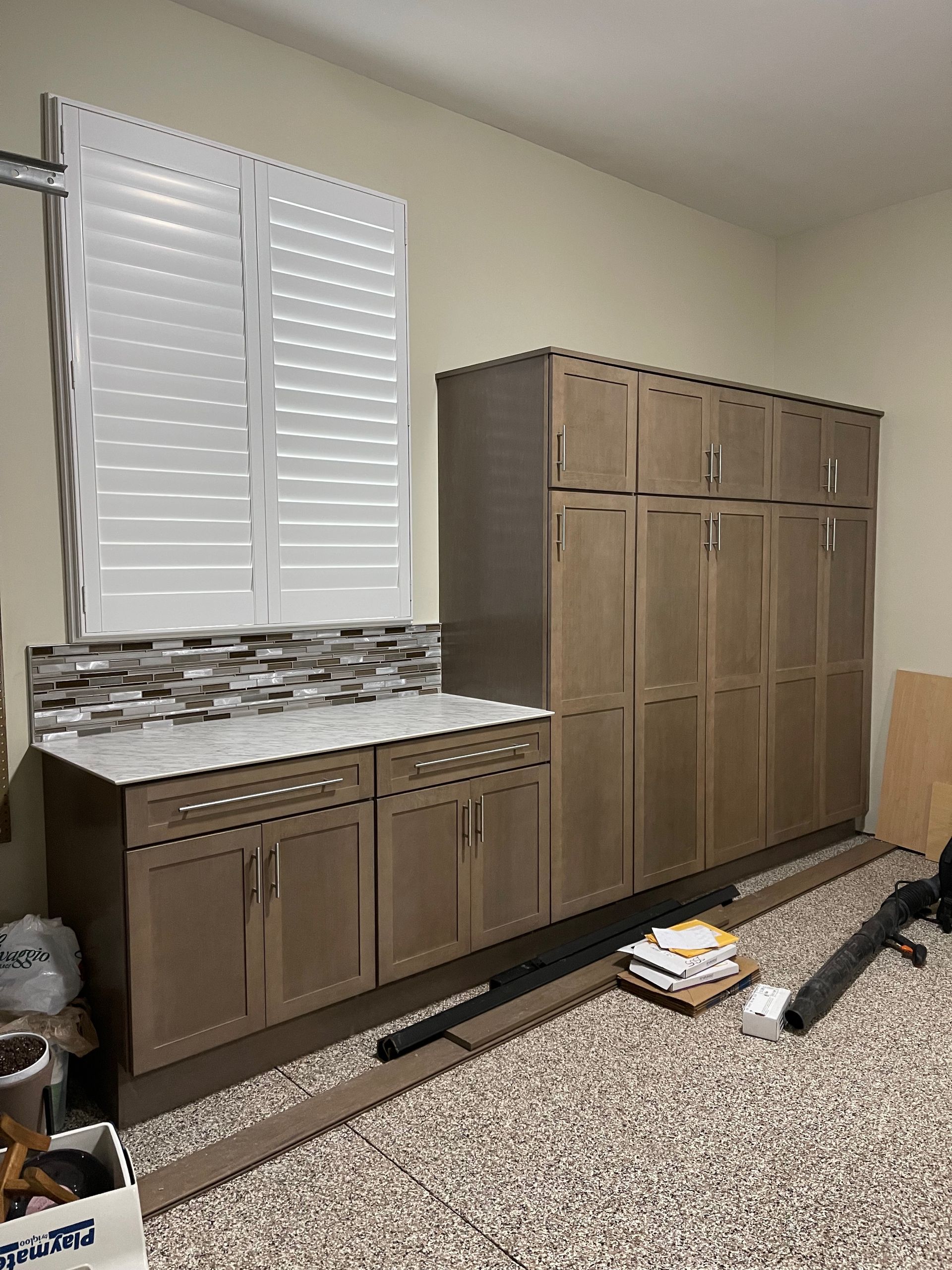 Cabinets against a wall with a window, countertop, and assorted items on the floor.