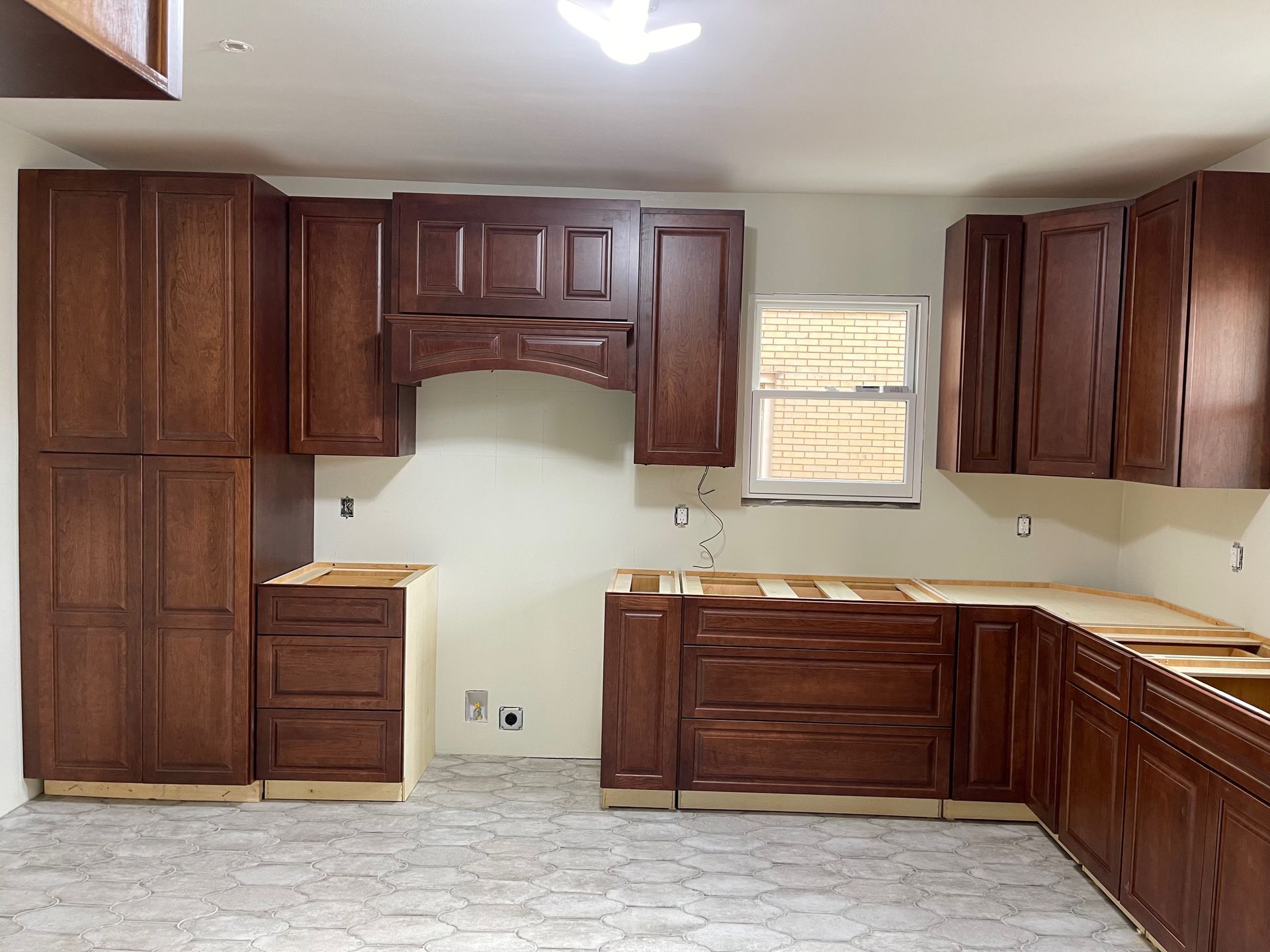 Kitchen cabinets, medium brown, installed against white walls, countertop space visible, window.