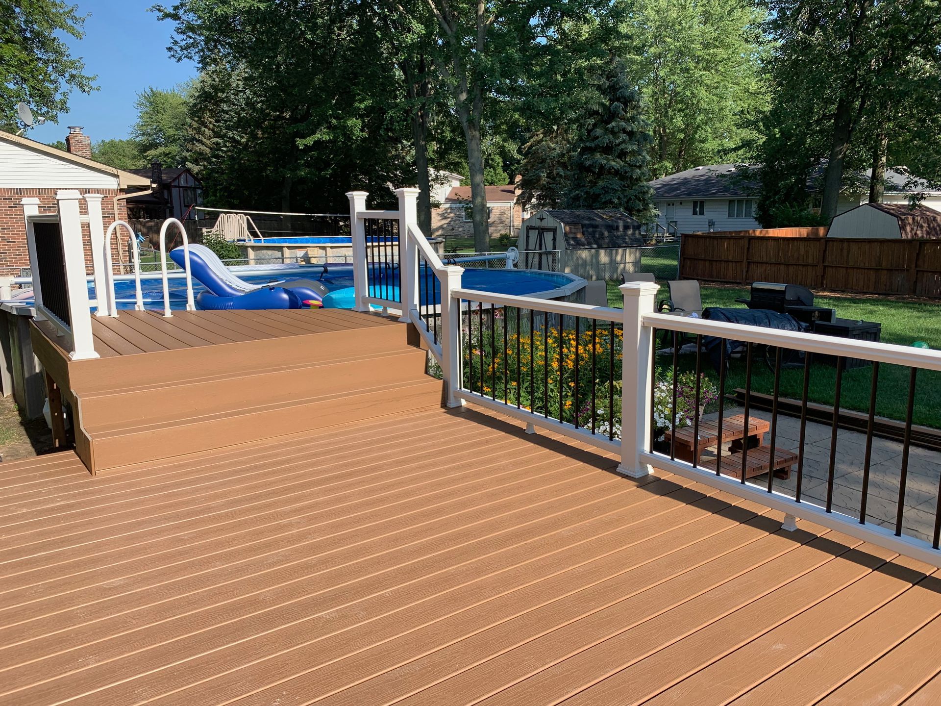 Brown deck with white railing overlooks backyard with two pools.