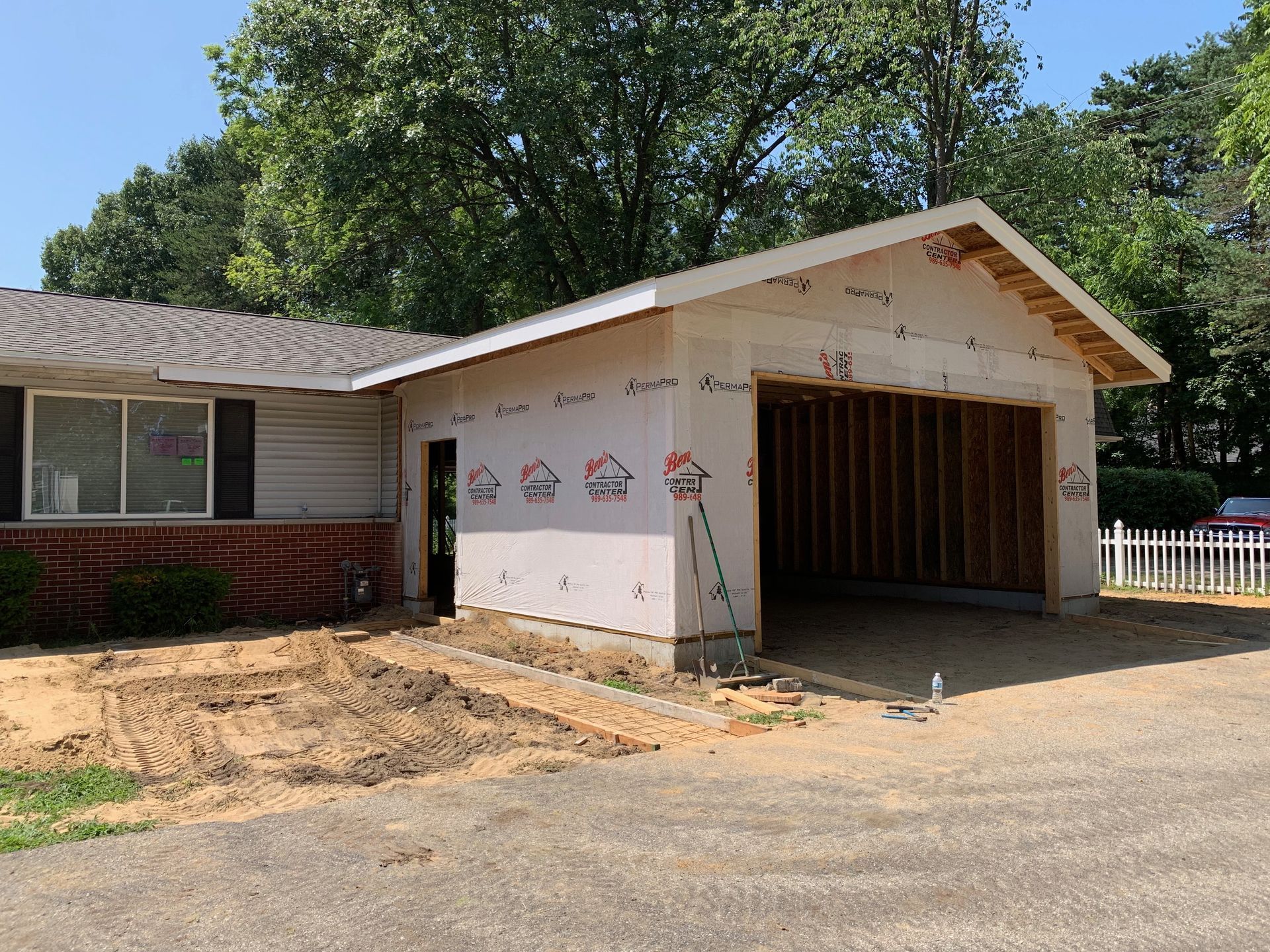Garage addition under construction next to a house with exposed framing and weather-resistant barrier.