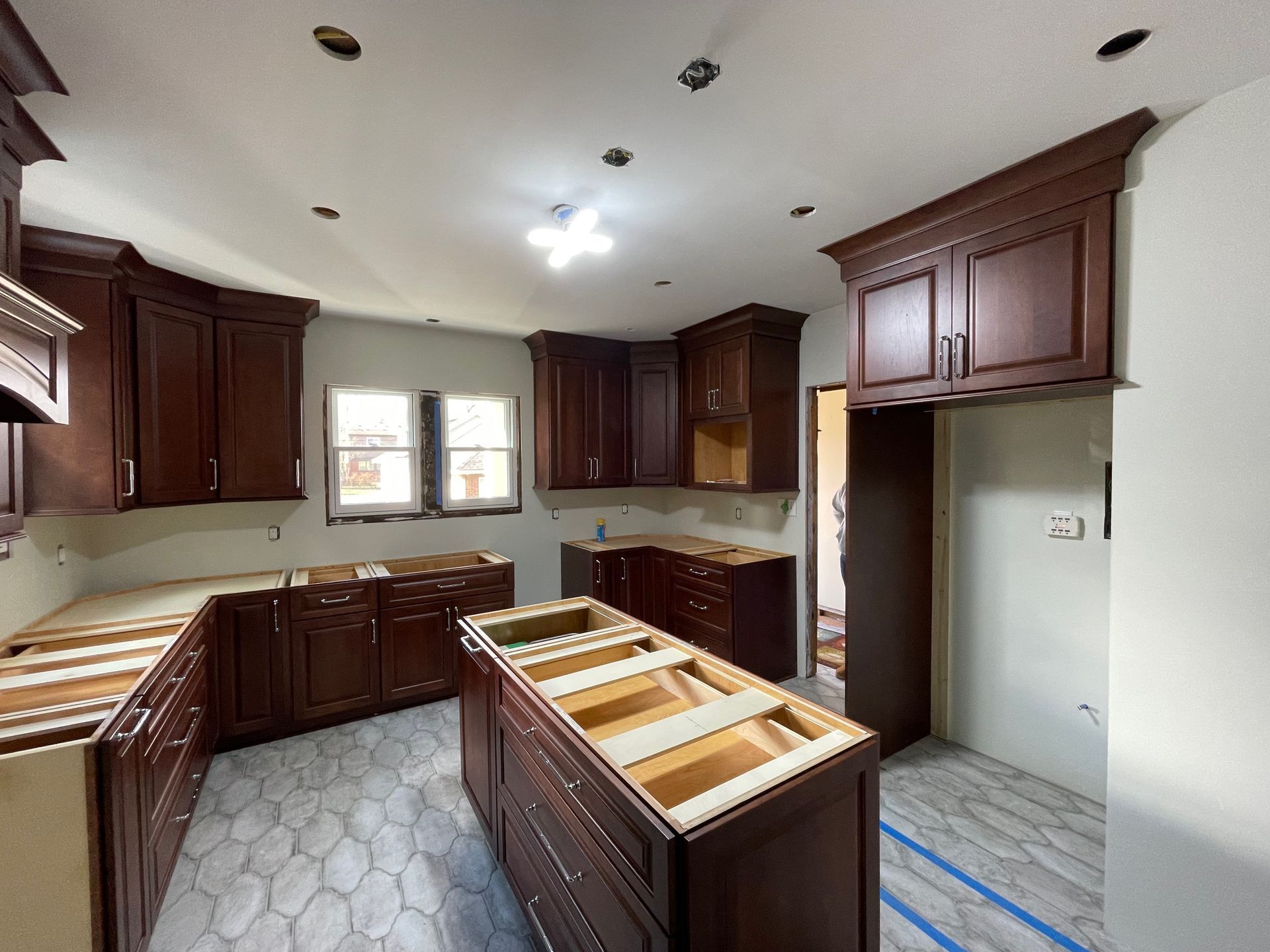 Kitchen under construction with brown cabinets, island, and grey and white patterned floor.