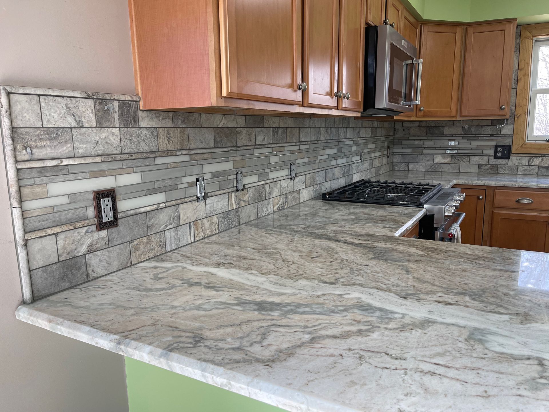 Kitchen with granite countertop and stone tile backsplash, wood cabinets.