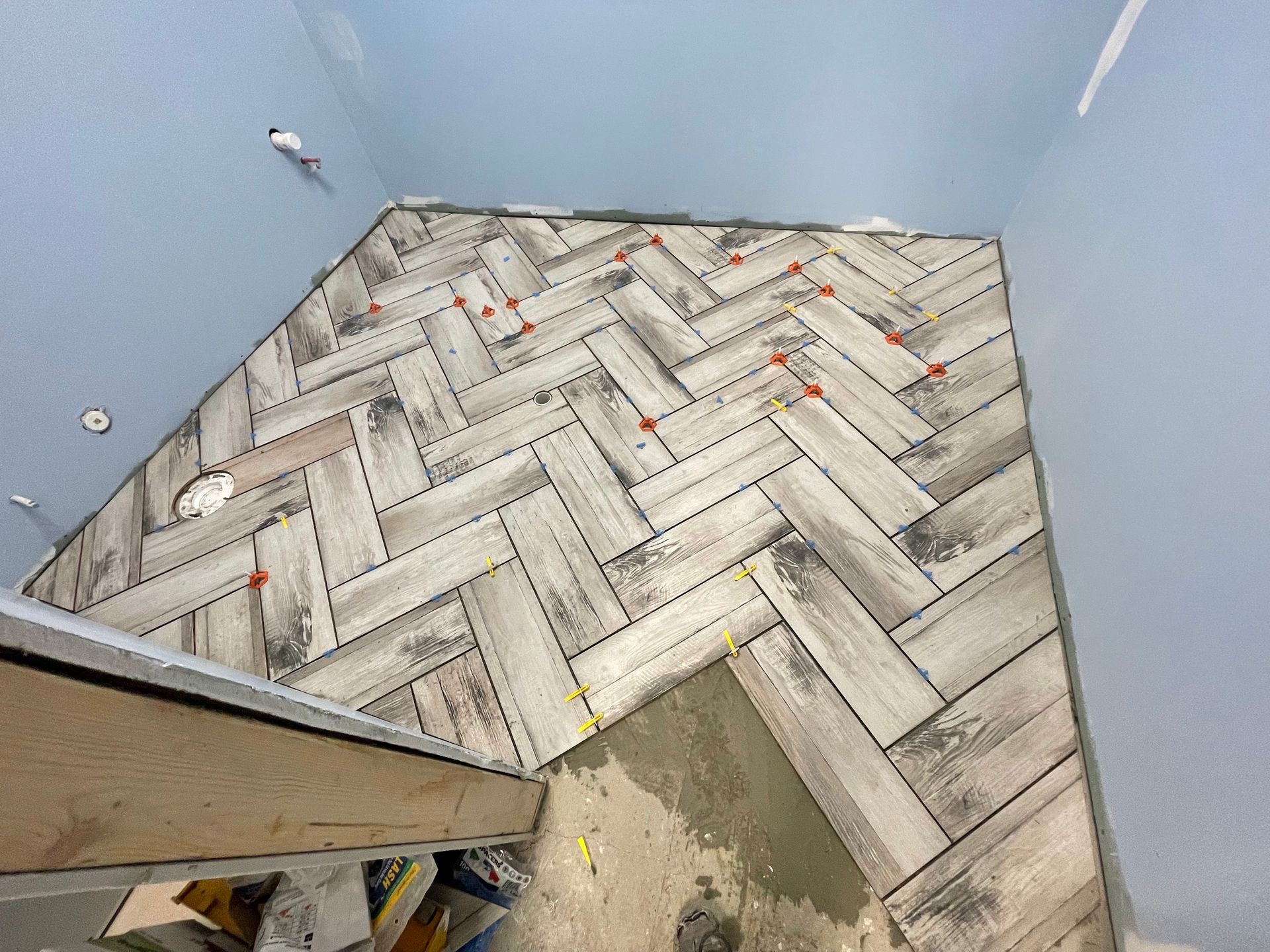 Herringbone pattern floor tiles being installed in a room with blue walls.