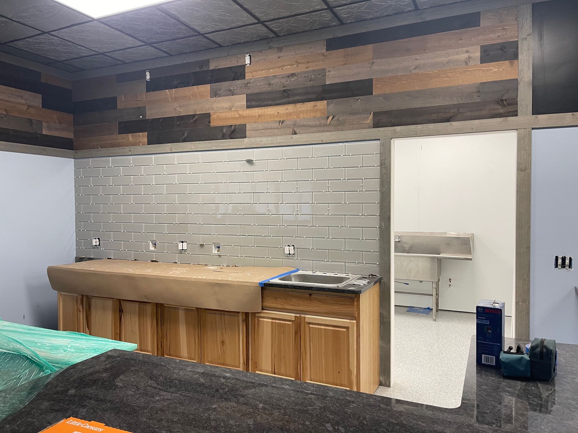 Interior view of a room under renovation, with wood and tile wall finishes, cabinets, and a doorway.