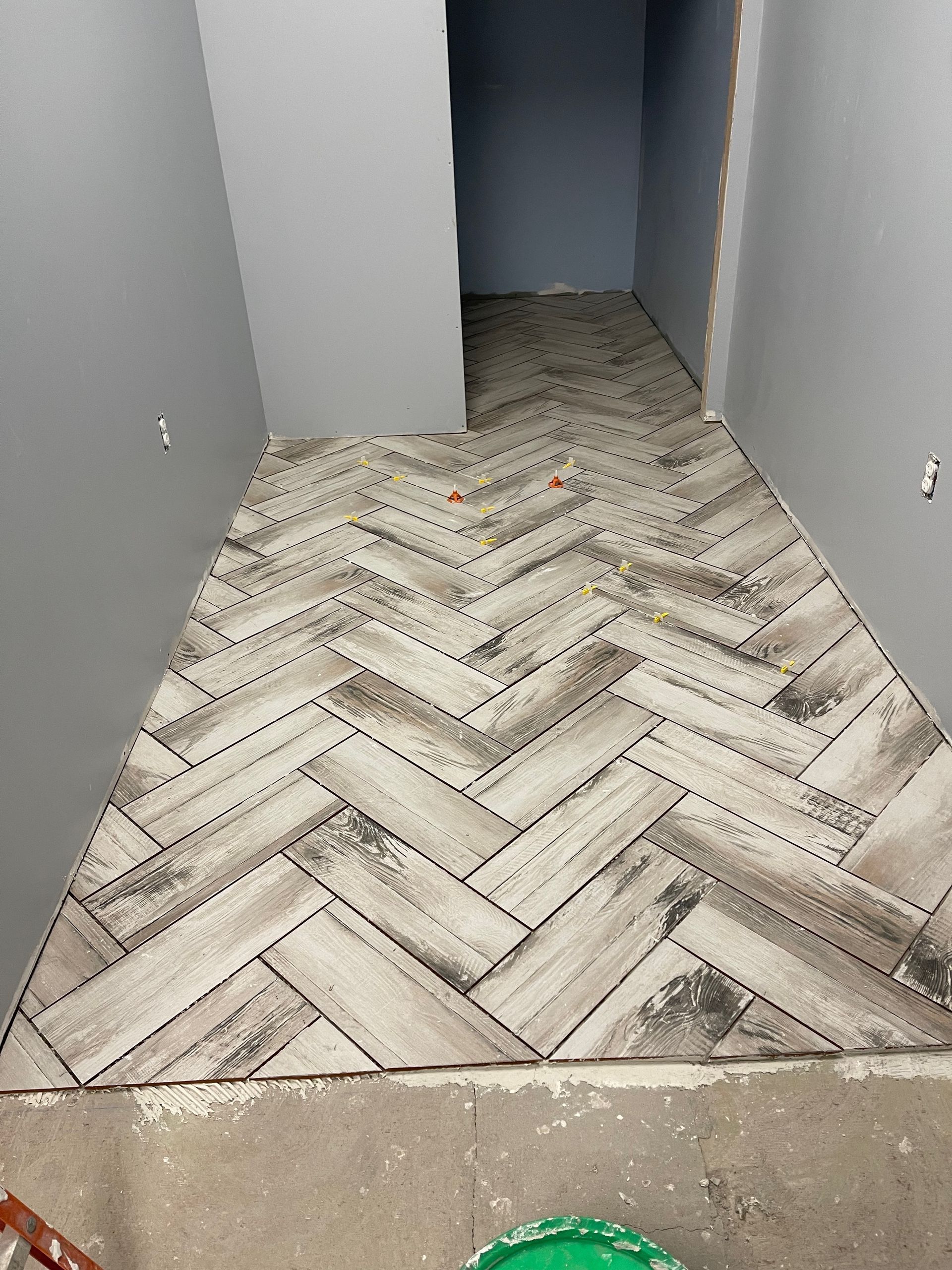 Herringbone tile floor in a hallway, installed against gray walls.