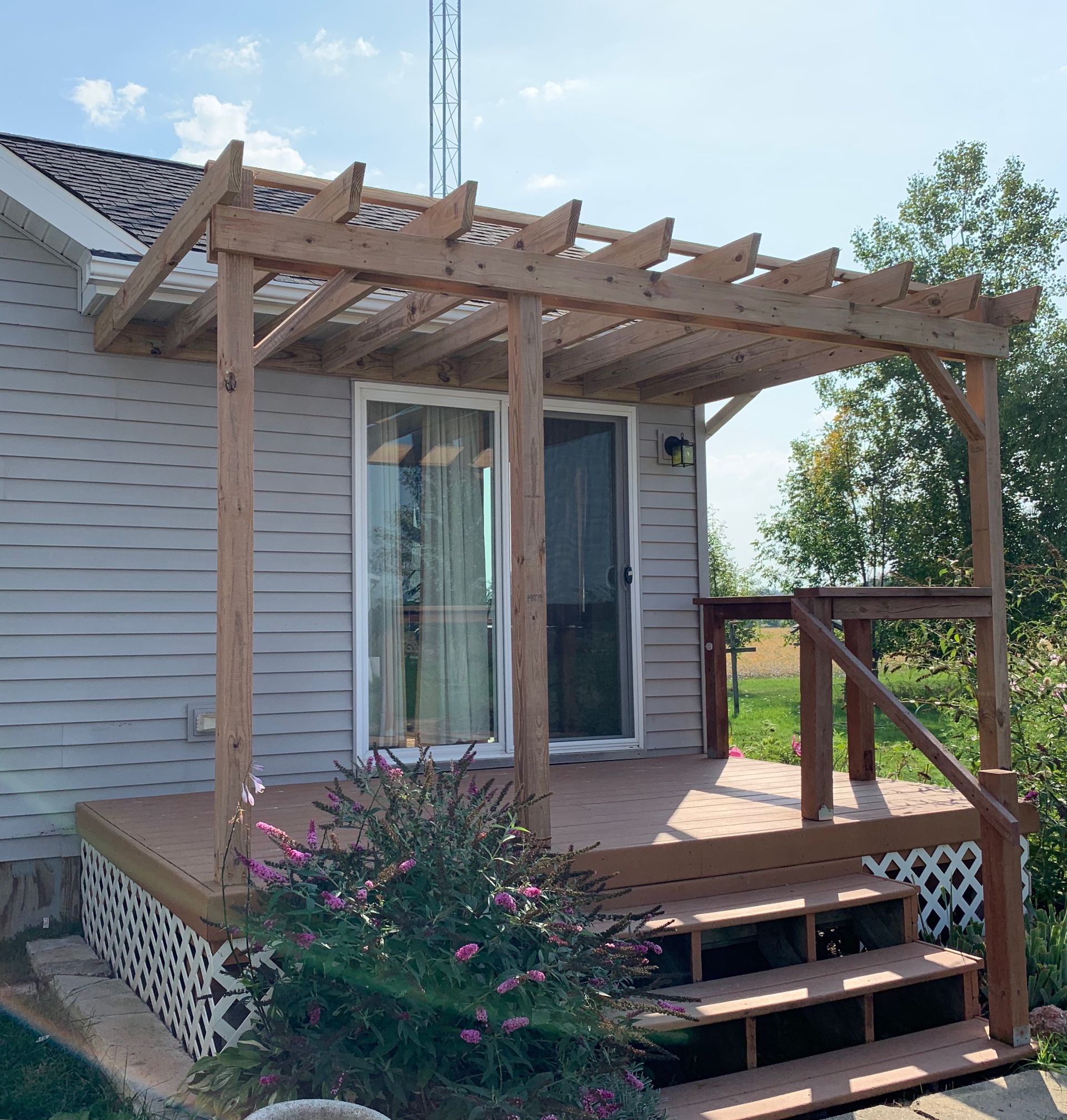 Wooden pergola over a deck with sliding glass doors, steps, and a handrail.