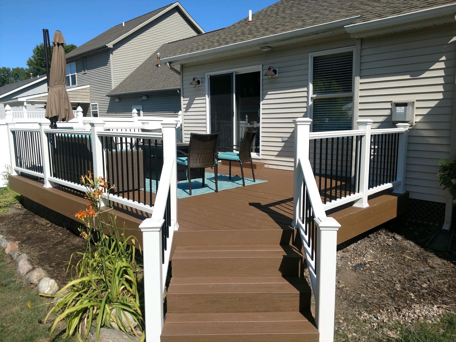 Brown deck with white railing, black spindles, leading to a house with a sliding glass door.