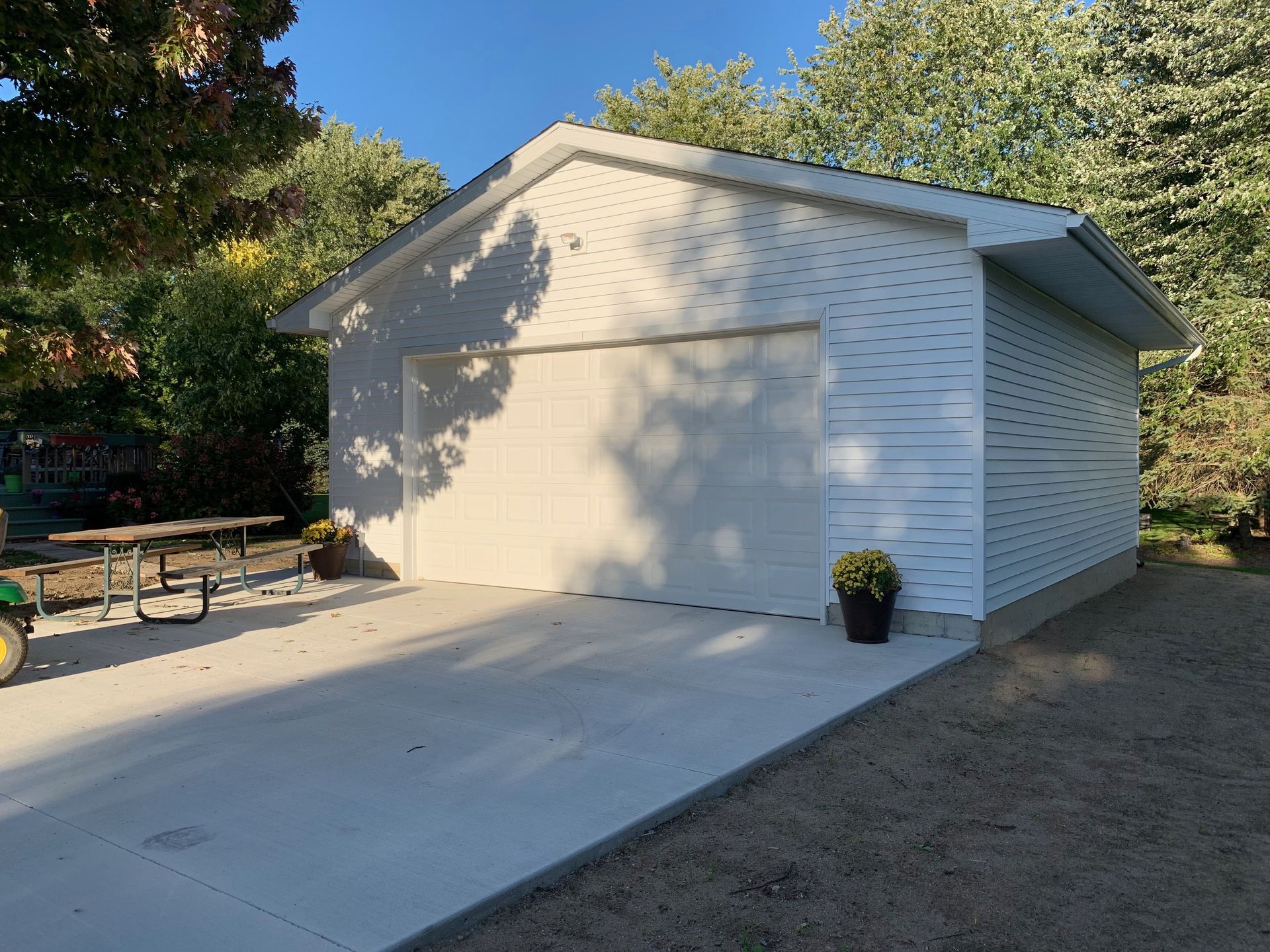 White-sided detached garage with concrete driveway on a sunny day.