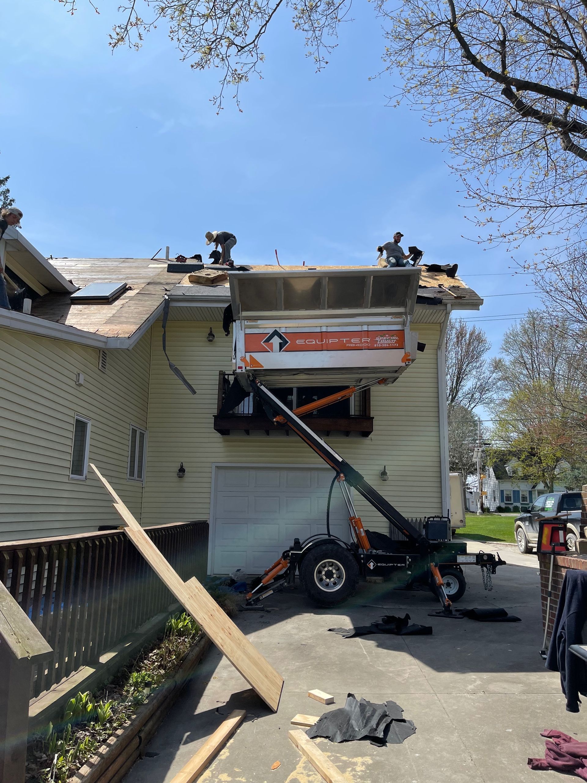 A house roof is being repaired, with a trailer-mounted hoist delivering supplies to the roof.