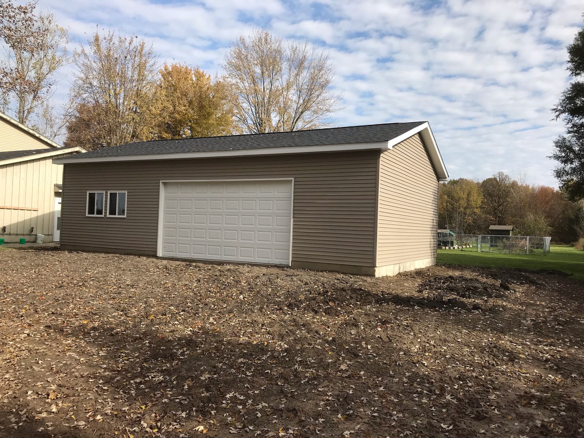 Tan-sided garage with white garage door and small window, set in a brown yard.