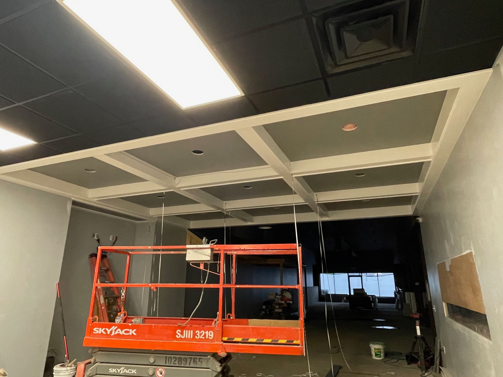 Interior view of a construction site with a coffered ceiling. An orange lift sits below.