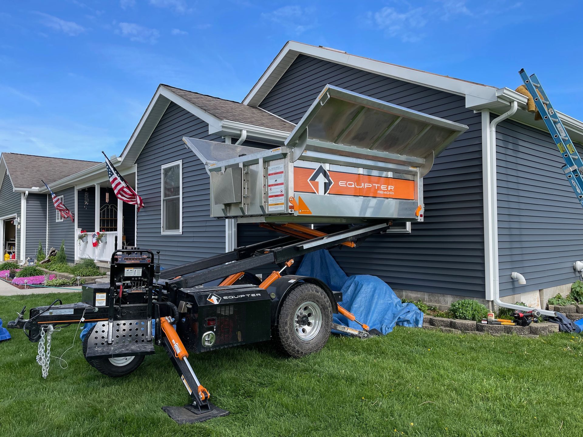 Roofing debris removal system trailer next to a house with blue siding.