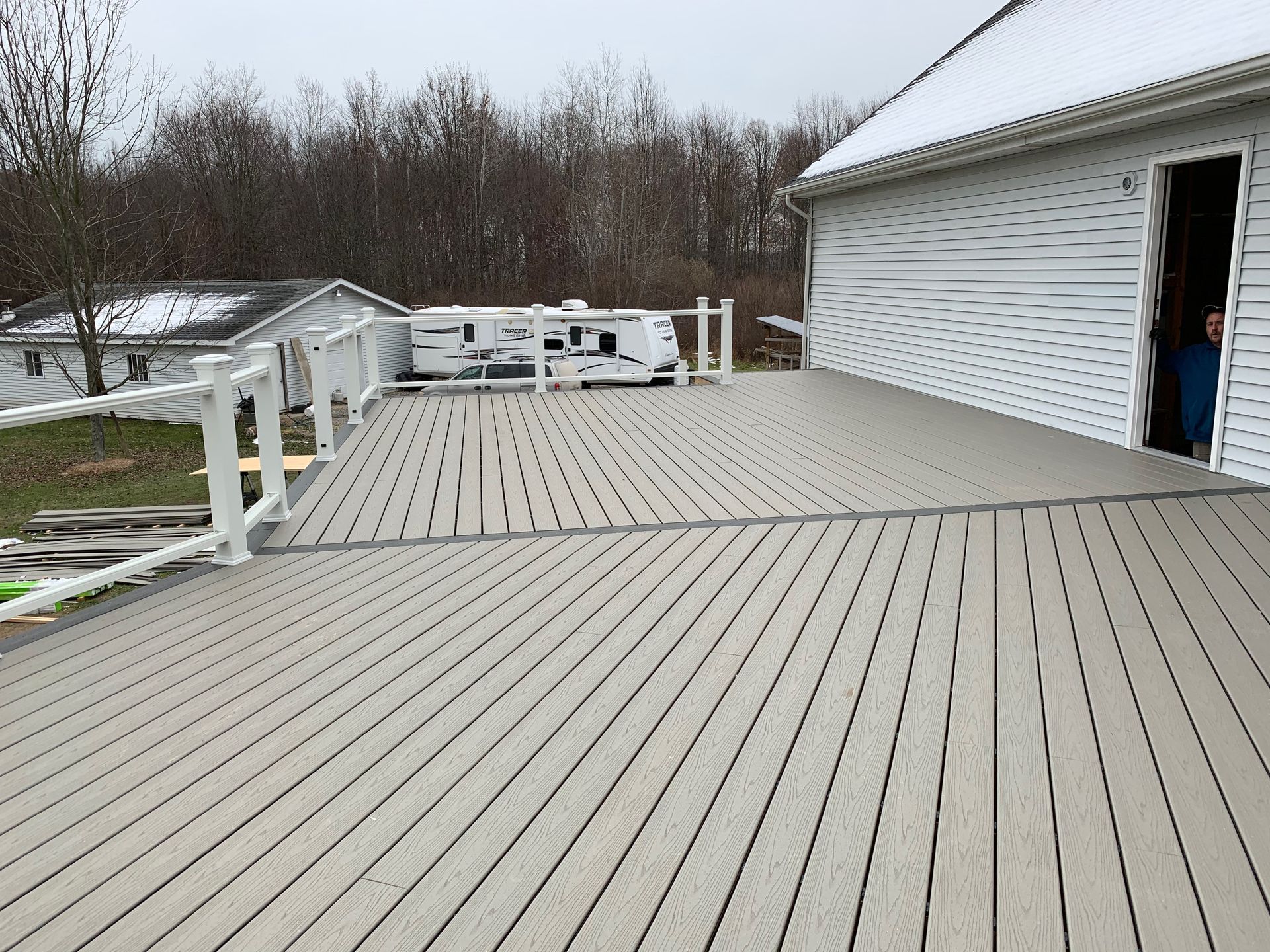 Large composite deck with white railing, RV in the background, next to a white house with an open door.