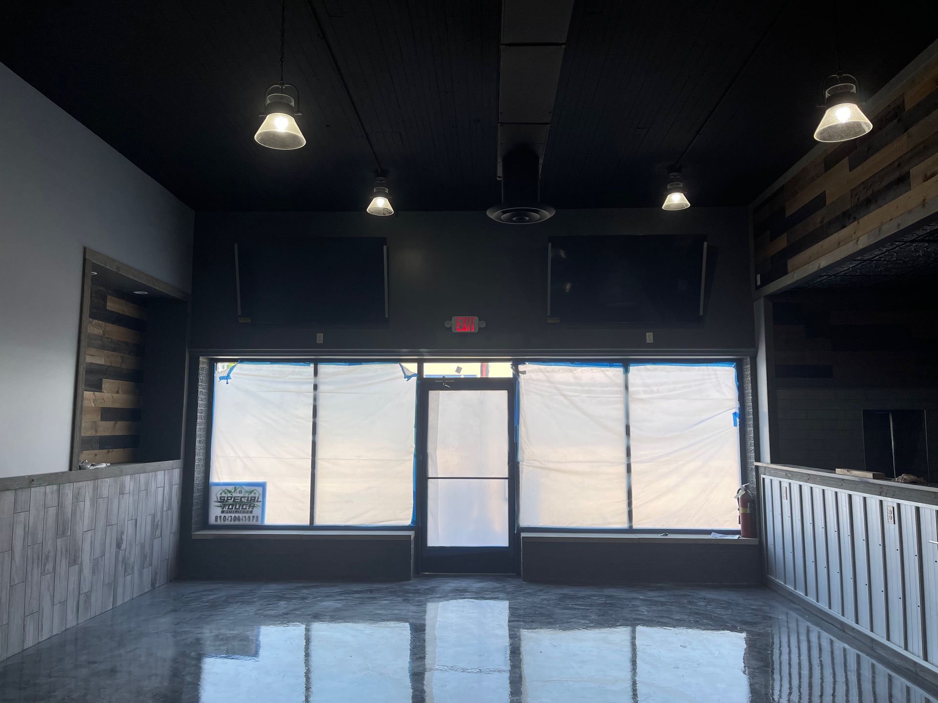 Empty interior, front windows covered. Black ceiling, dark grey walls, exposed wood accents, concrete floor.