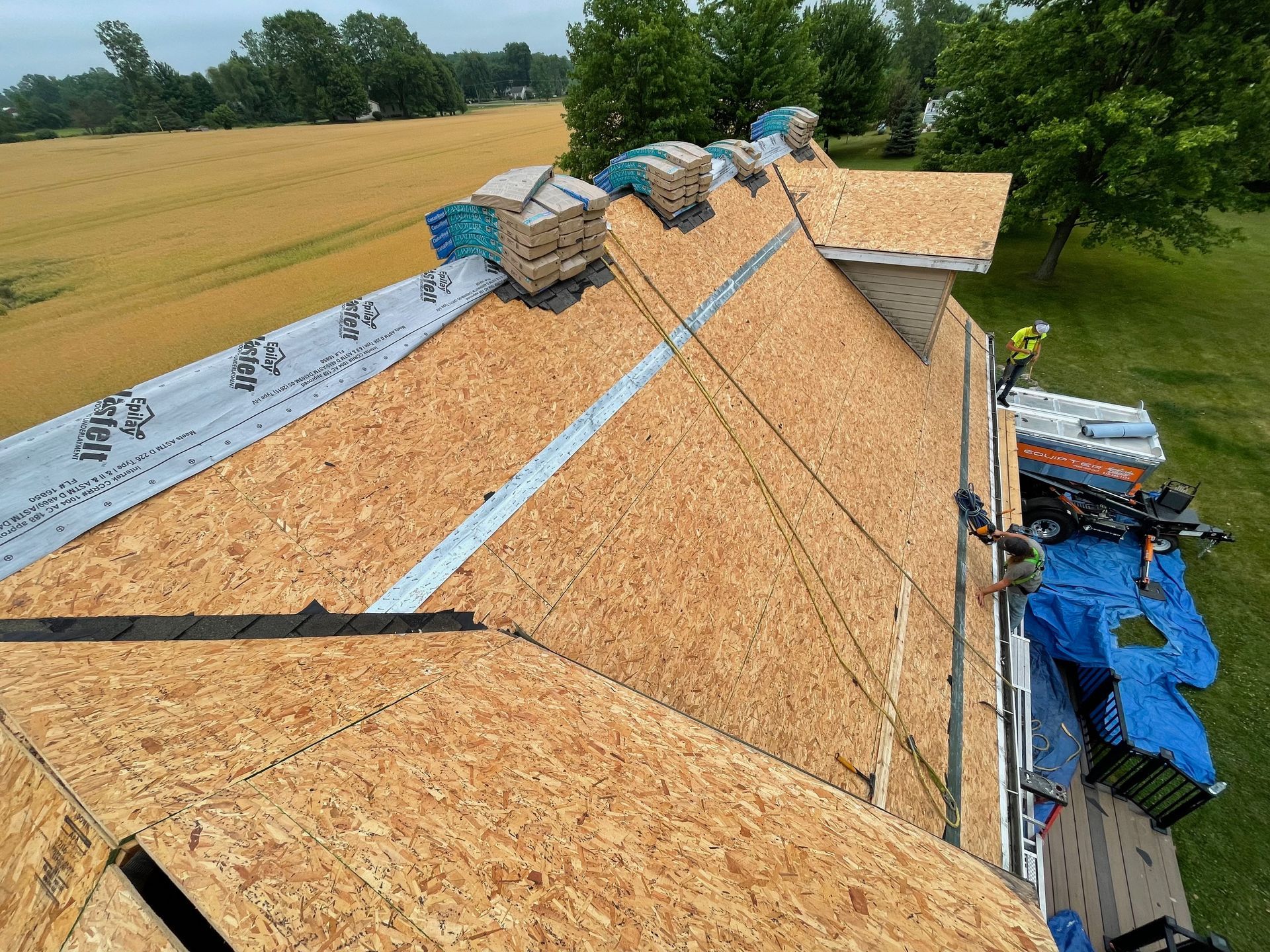 Roofing construction, with workers on a partly shingled roof and materials laid out.