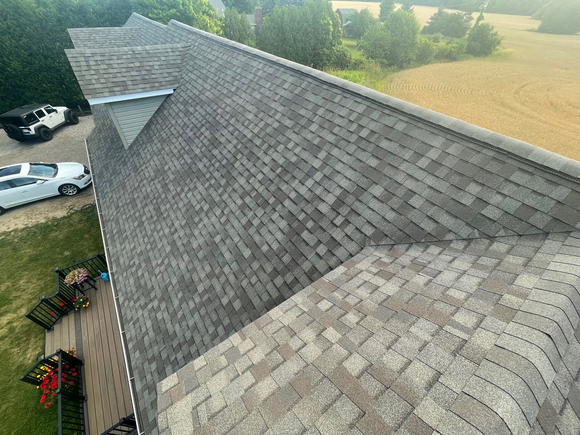 Overhead view of a house roof with gray shingles. Cars and green yard are visible.
