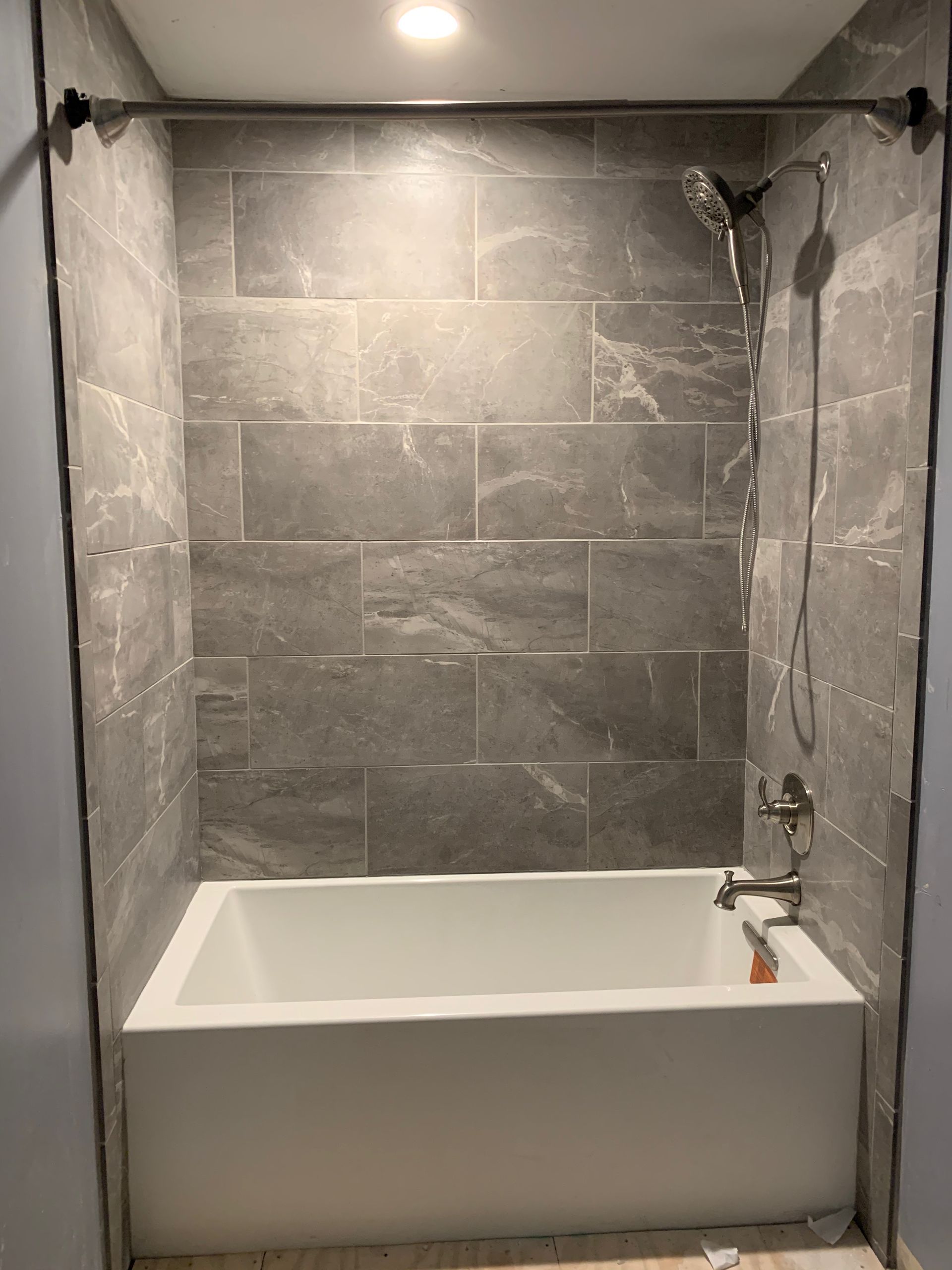 Newly tiled bathroom with a white tub and shower fixtures. Gray tiles cover the walls.