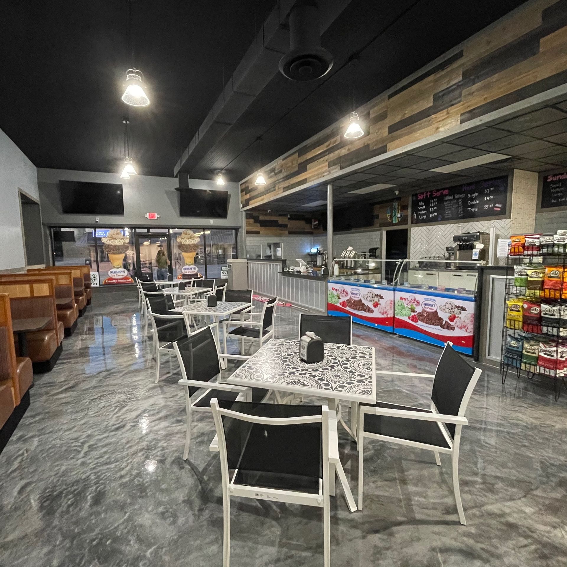 Interior of a cafe with tables and chairs, a dessert display, and snacks for sale.