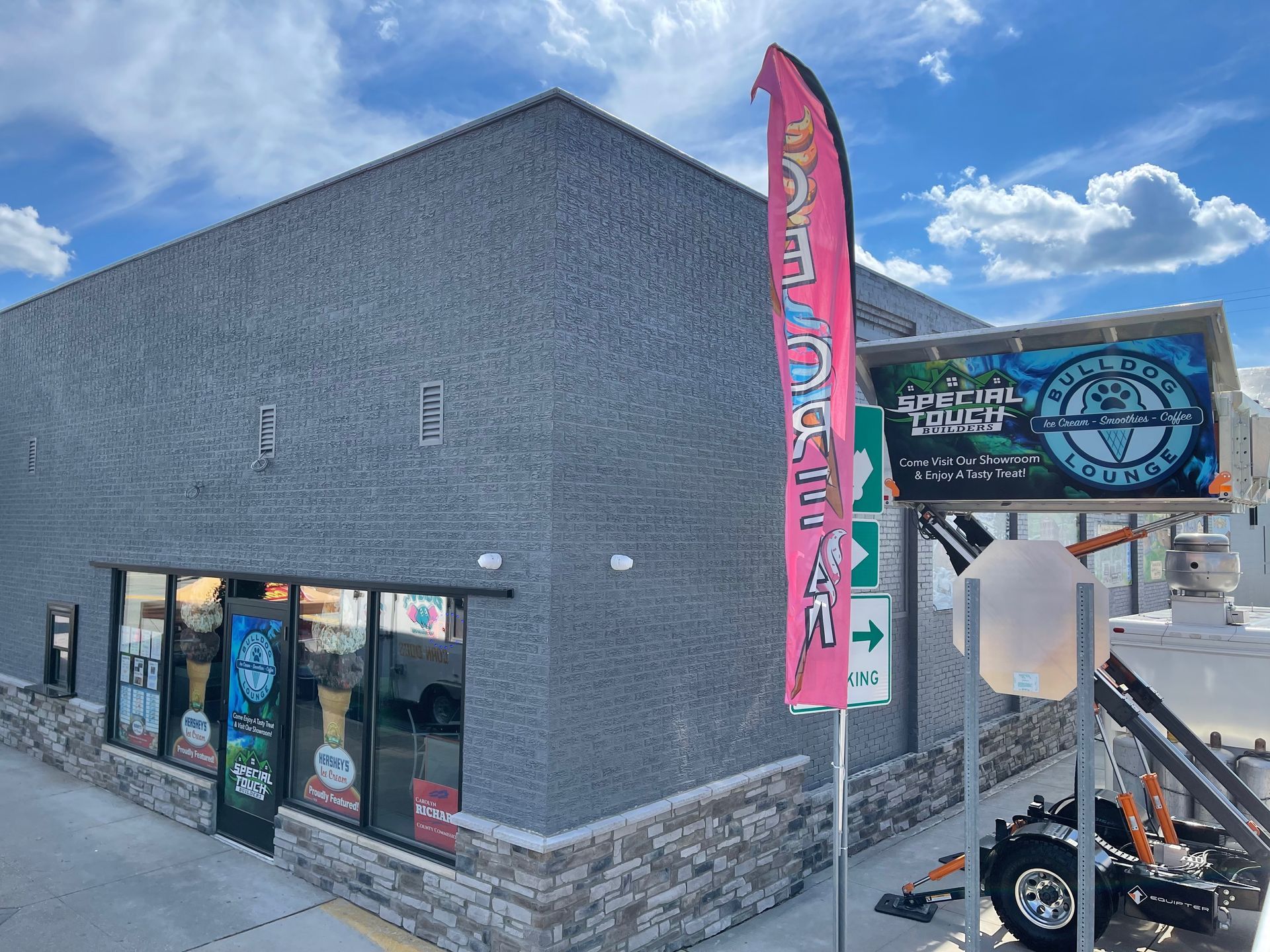 Storefront with a pink flag, sign, and display window. Building exterior with stone and gray facade.