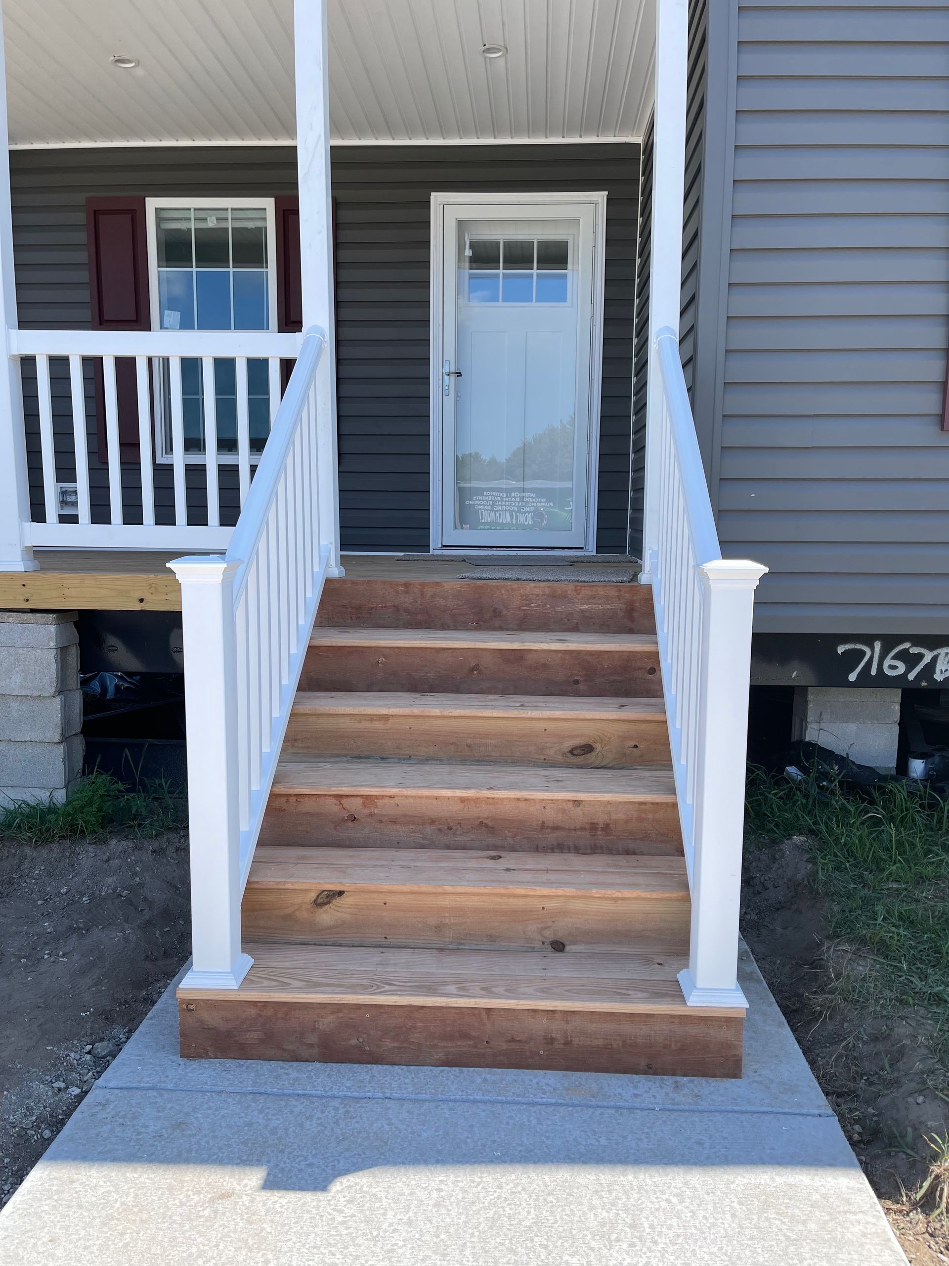 Wooden stairs leading to a white door, framed by a white railing and gray siding.