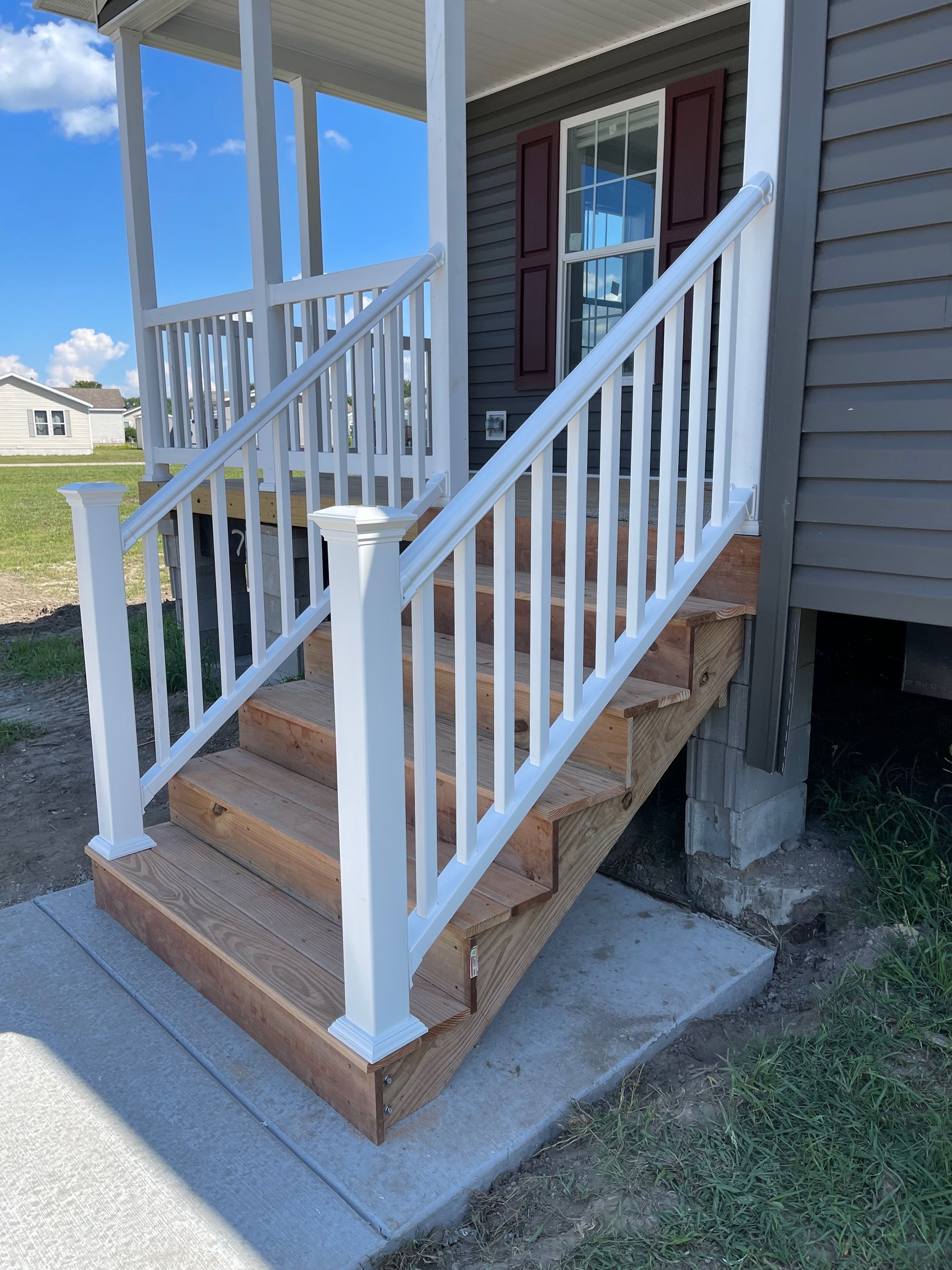 White-railed wooden stairs leading to a porch entrance. Grey siding on the house, blue sky above.