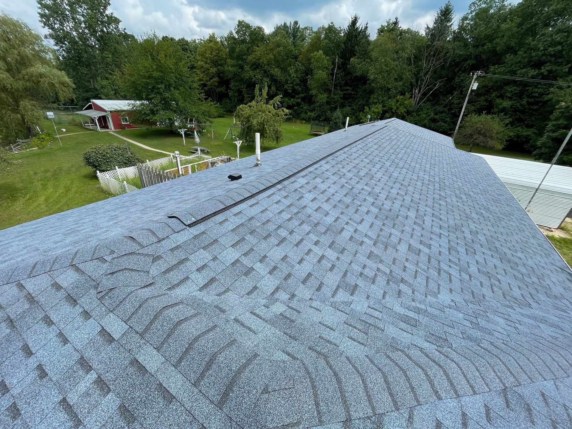 Gray shingle roof, green yard, and trees in background.