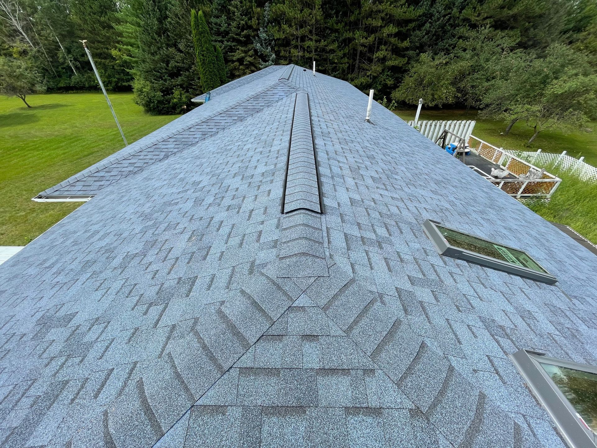 Overhead view of a blue shingle roof with a vent and skylights in a grassy yard.