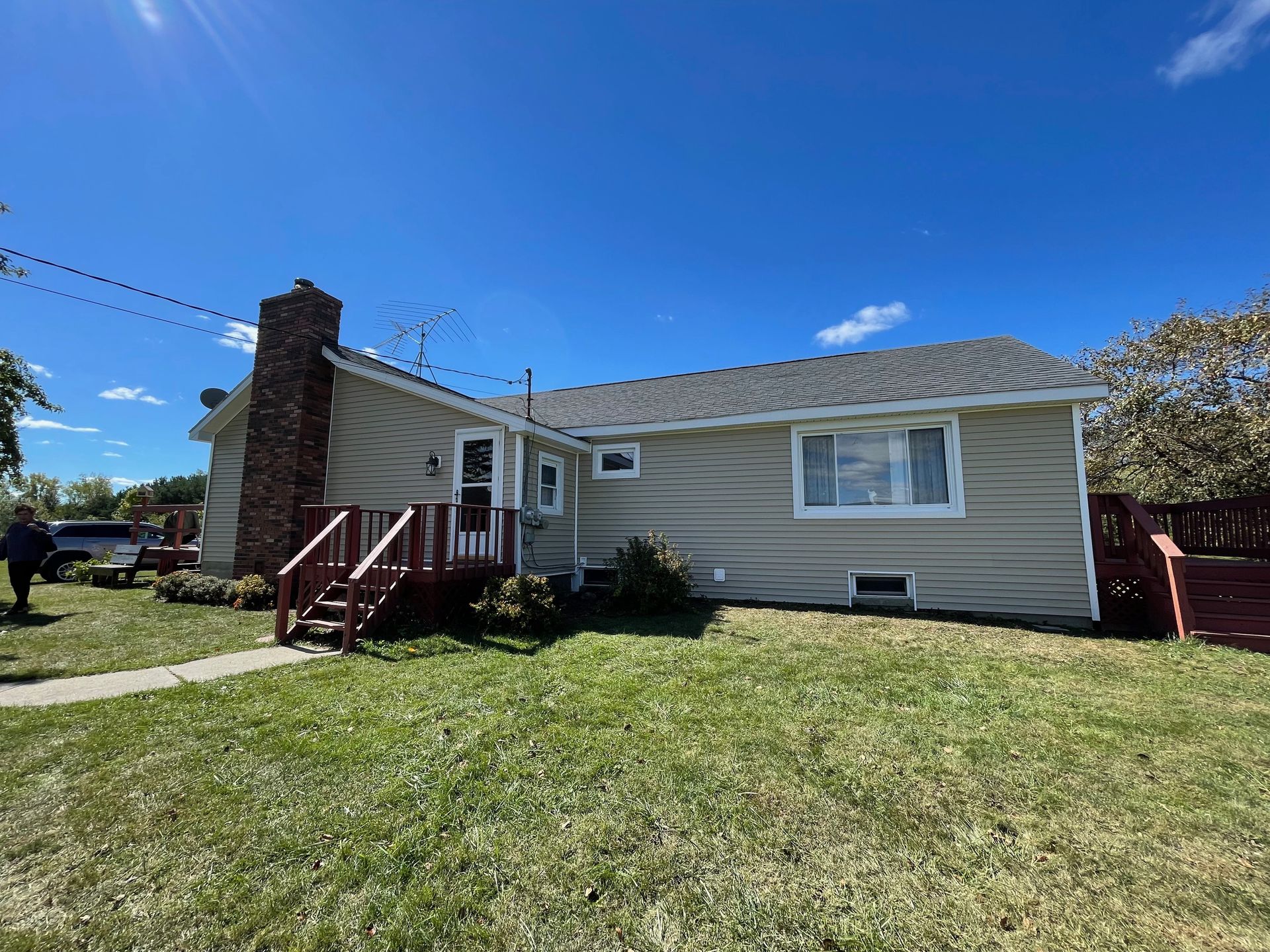Tan house with a red chimney, porch, and fence on a green lawn under a blue sky.