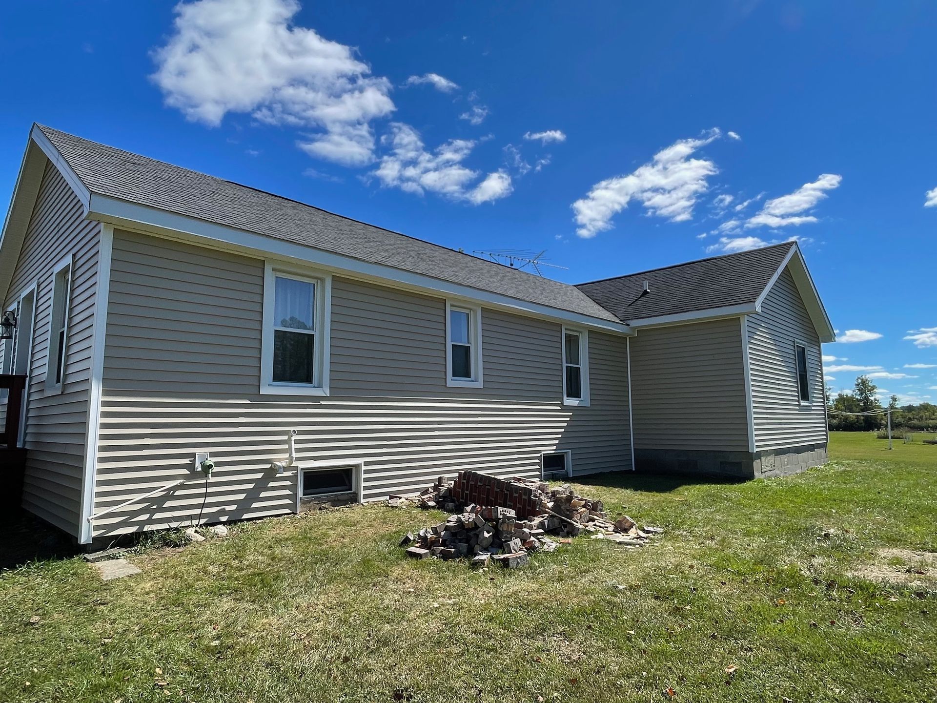 Tan house with gray roof on a grassy field under a blue sky with clouds.