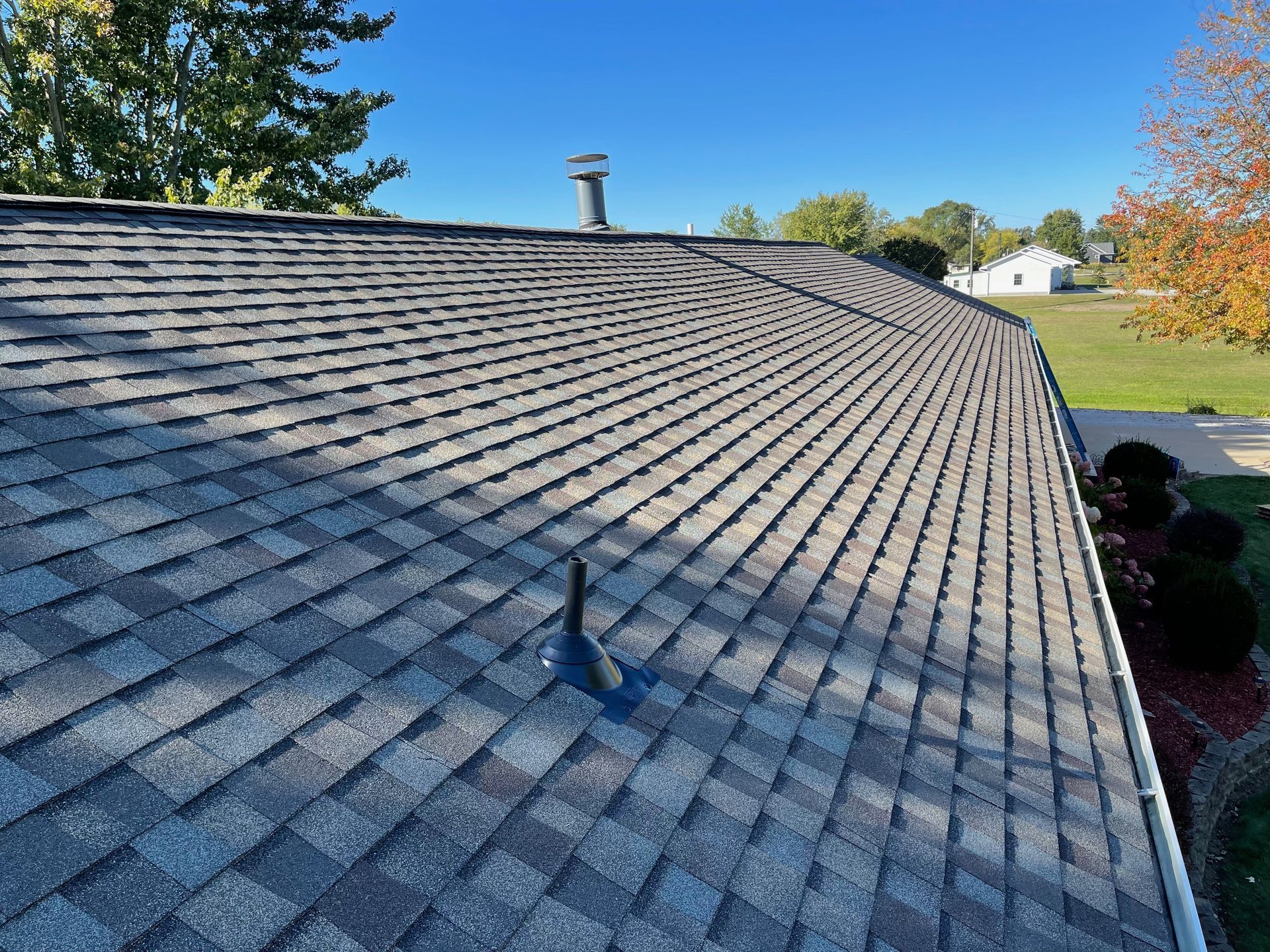 Gray asphalt shingle roof on a house, clear blue sky overhead.