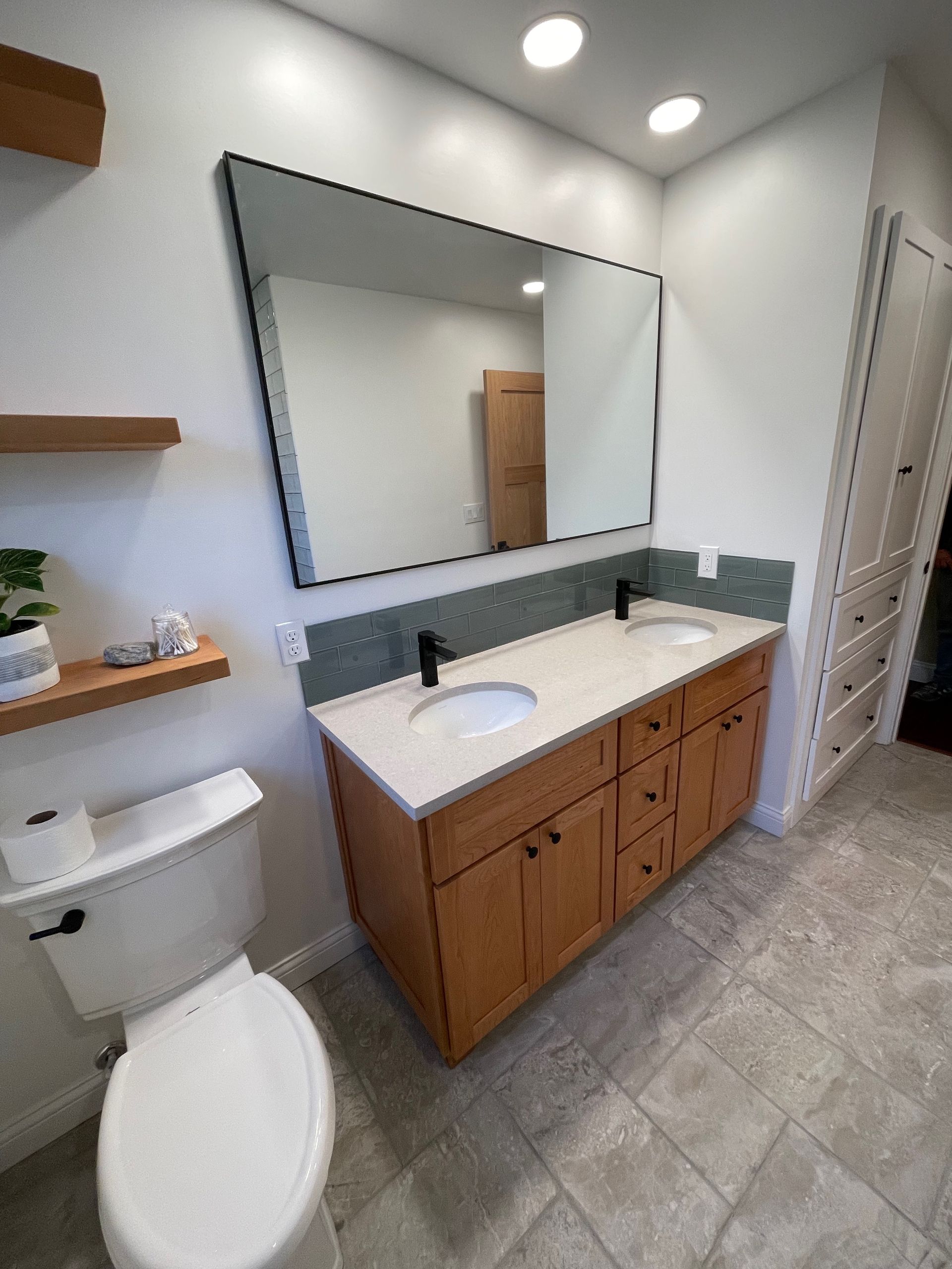 Bathroom with a double vanity, large mirror, and toilet. Light wood cabinets, white countertops, gray tile floor.